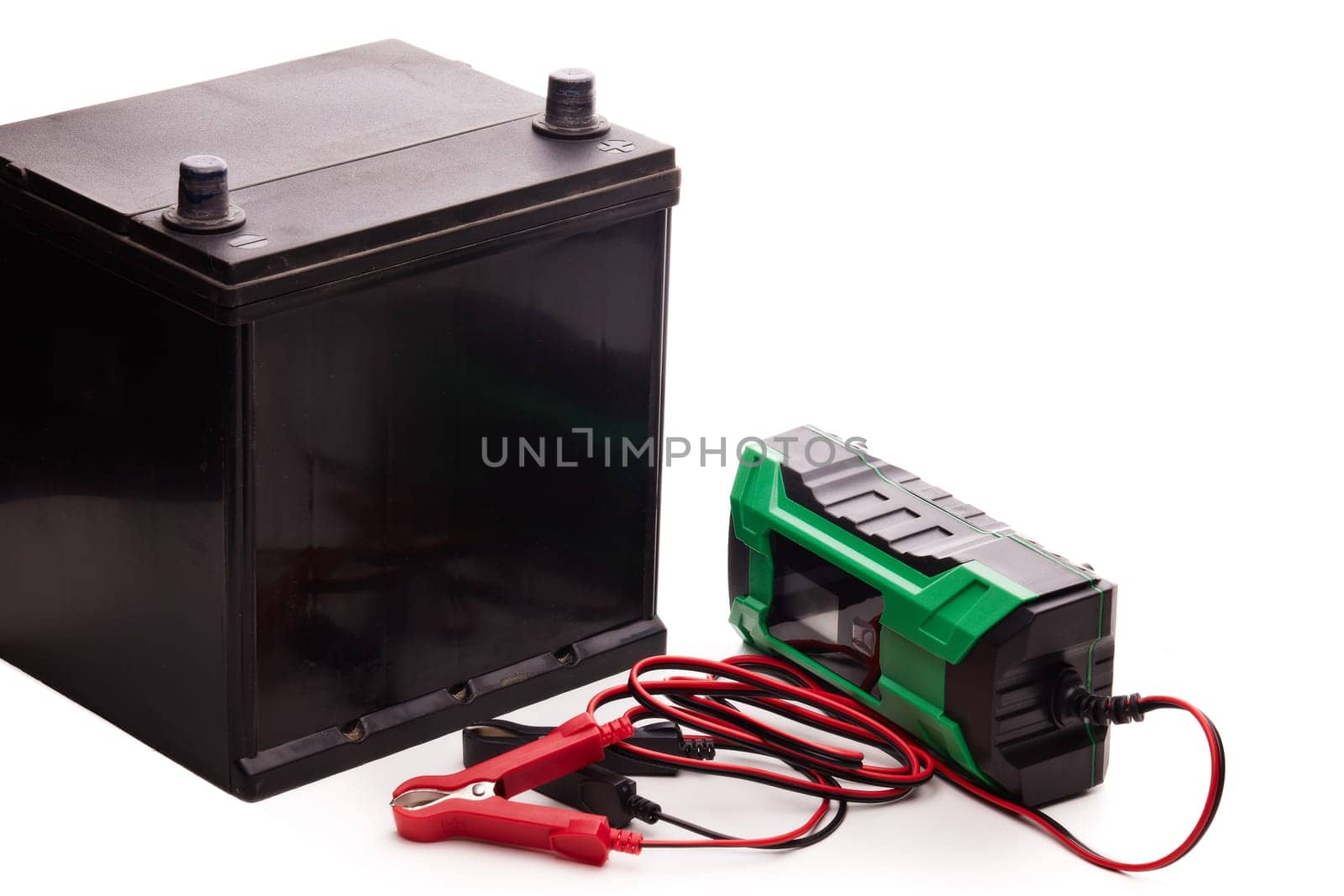 Black car accumulator battery and green charger isolated on a white background. Acid battery,12 volts supply. Concept of service, maintenance, charging car battery, diy