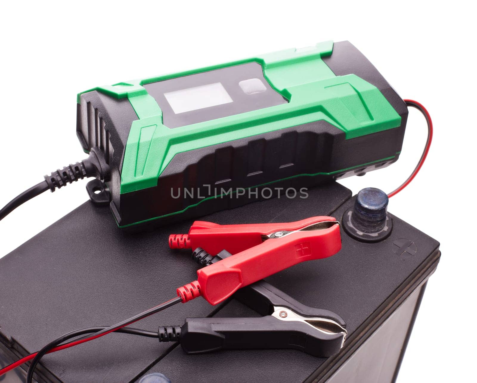 Black car accumulator battery and green charger isolated on a white background. Top view. Acid battery,12 volts supply. Concept of service, maintenance, charging car battery, diy
