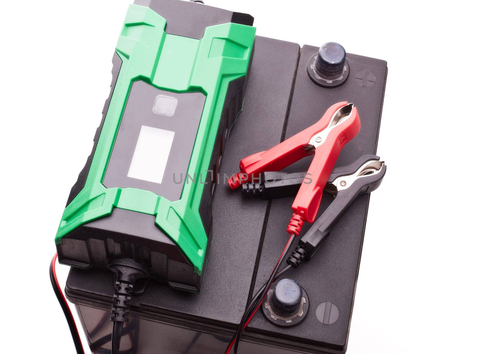 Black car accumulator battery and green charger isolated on a white background. Top view. Acid battery,12 volts supply. Concept of service, maintenance, charging car battery, diy