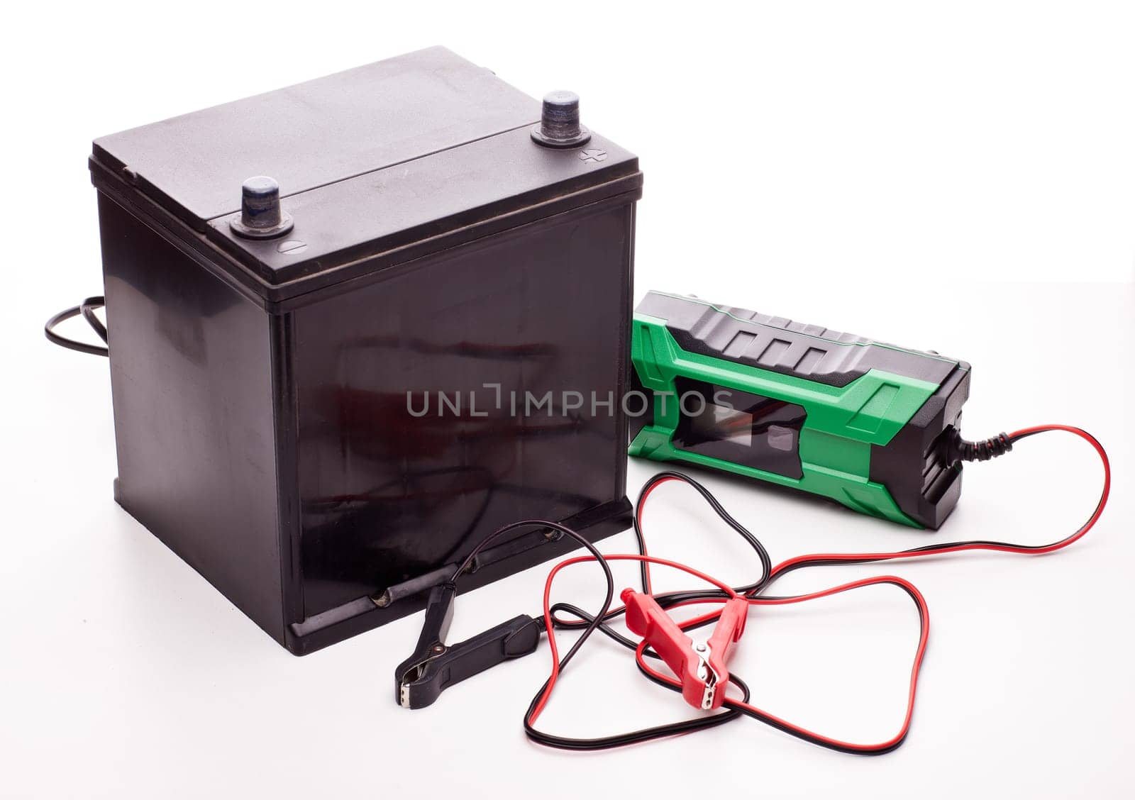 Black car accumulator battery and green charger isolated on a white background. Acid battery,12 volts supply. Concept of service, maintenance, charging car battery, diy