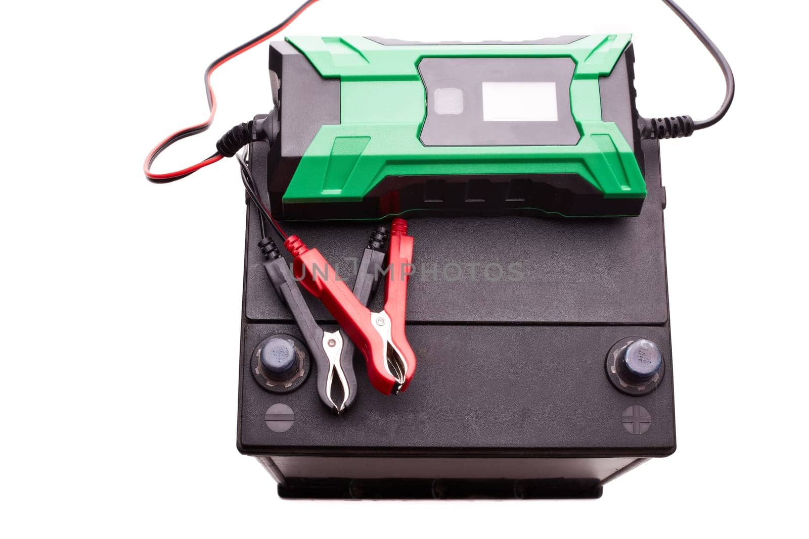 Black car accumulator battery and green charger isolated on a white background. Top view. Acid battery,12 volts supply. Concept of service, maintenance, charging car battery, diy