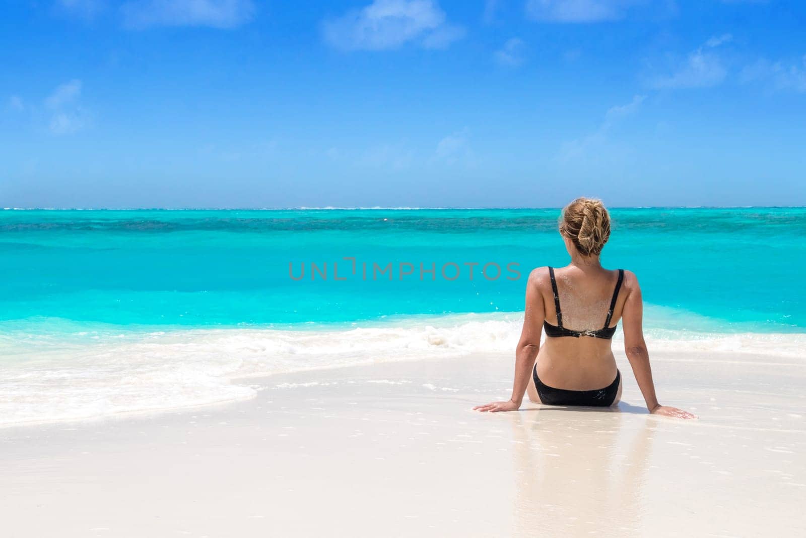 Blonde Girl in black bikini on dream beach at the turquoise ocean