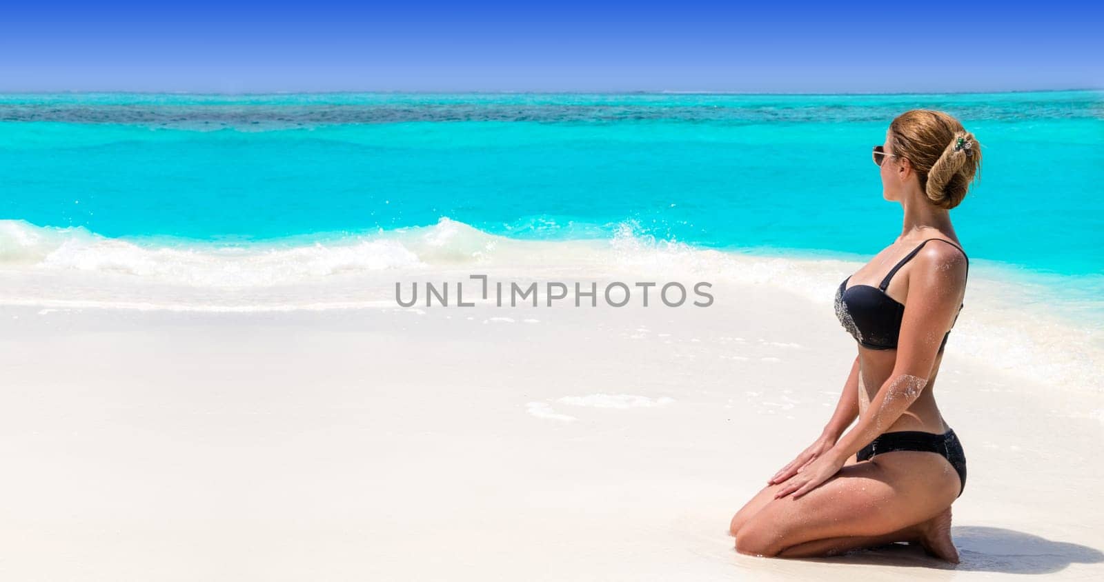 Blonde Girl in black bikini on dream beach at the turquoise ocean