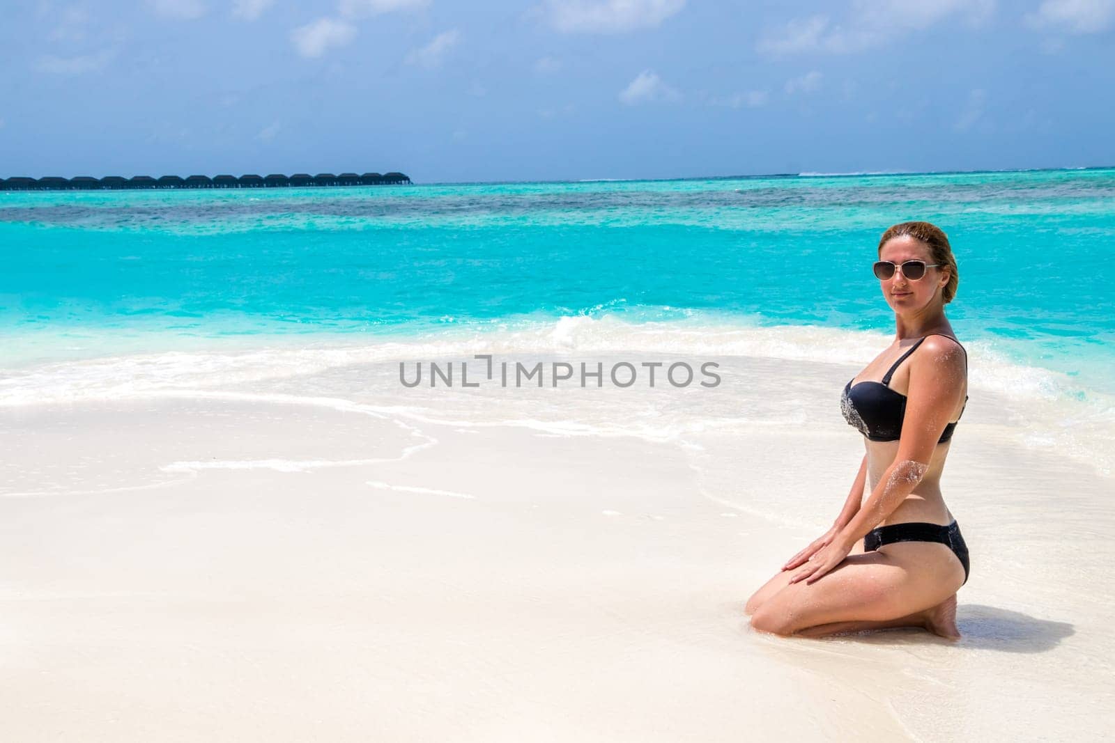Blonde Girl in black bikini on dream beach at the turquoise ocean