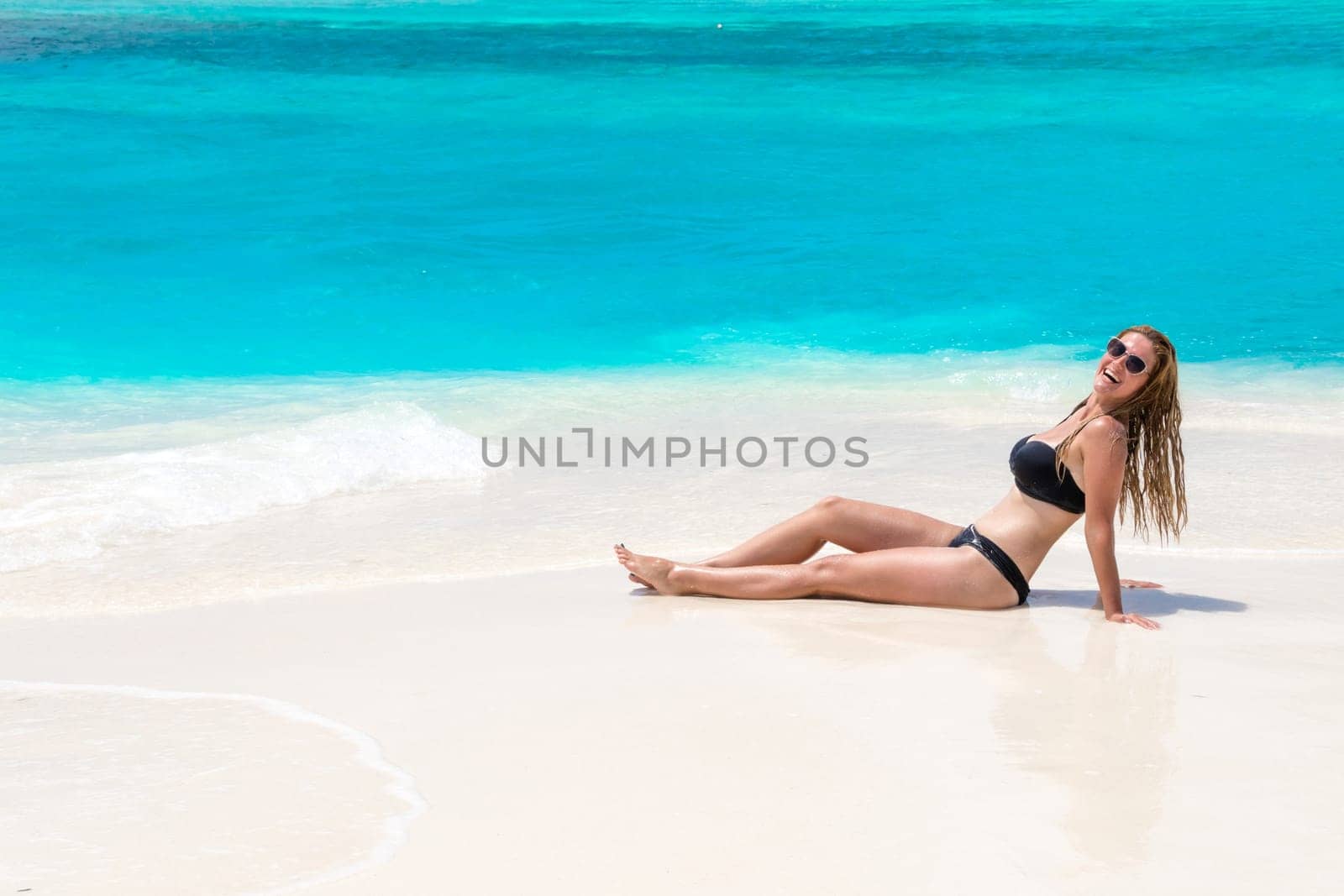 Blonde Girl in black bikini on dream beach at the turquoise ocean