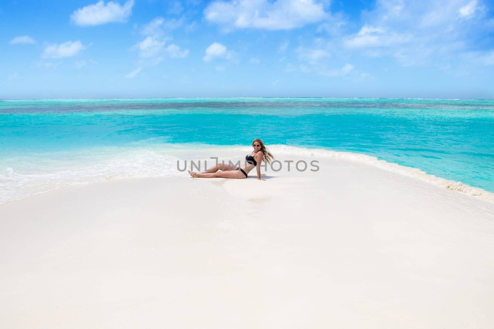 Blonde Girl in black bikini on dream beach at the turquoise ocean