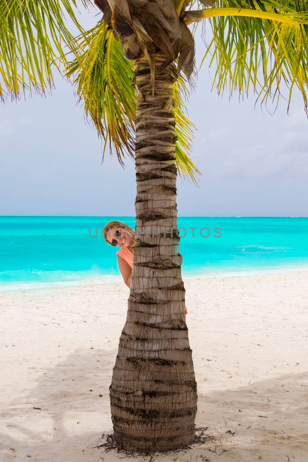 Gorgeous woman behind a palm tree at the dream beach