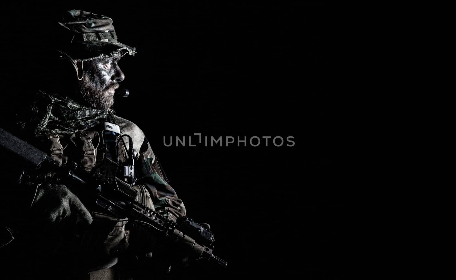 Bearded Special forces United States in Camouflage Uniforms studio shot half length black background. Holding weapons, wearing jungle hat, Shemagh scarf, he is ready to kill. Backlit