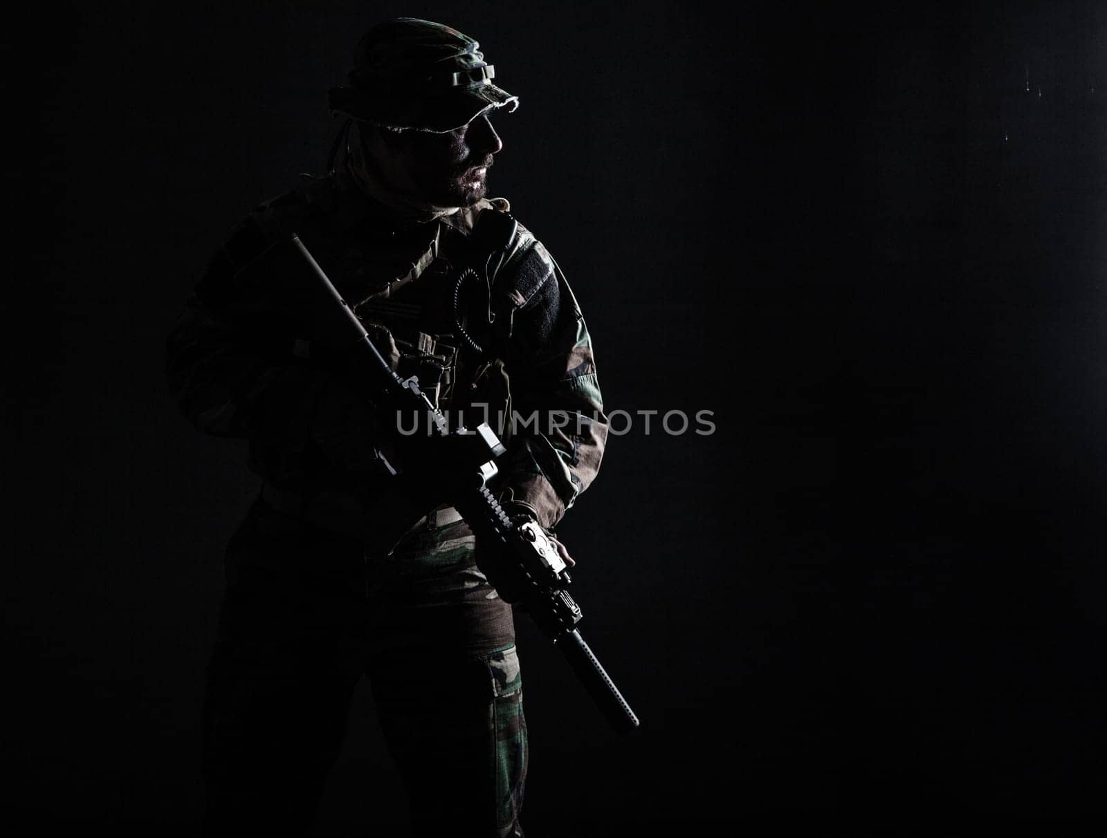Bearded Special forces United States in Camouflage Uniforms studio shot half length. Holding weapons, wearing jungle hat, Shemagh scarf, he is ready to kill. Contour shot, backlit
