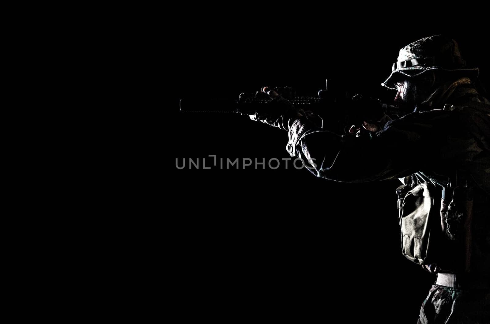 Bearded Special forces United States in Camouflage Uniforms studio shot half length black background, backlit. He is shooting killing enemy, pointing the rifle