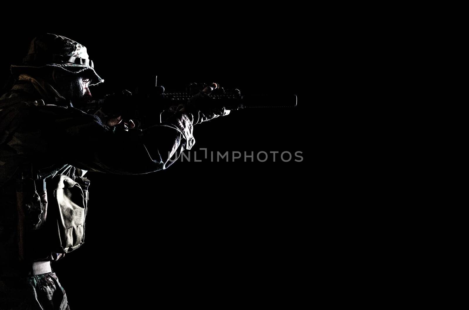 Bearded Special forces United States in Camouflage Uniforms studio shot half length black background, backlit. He is shooting killing enemy, pointing the rifle