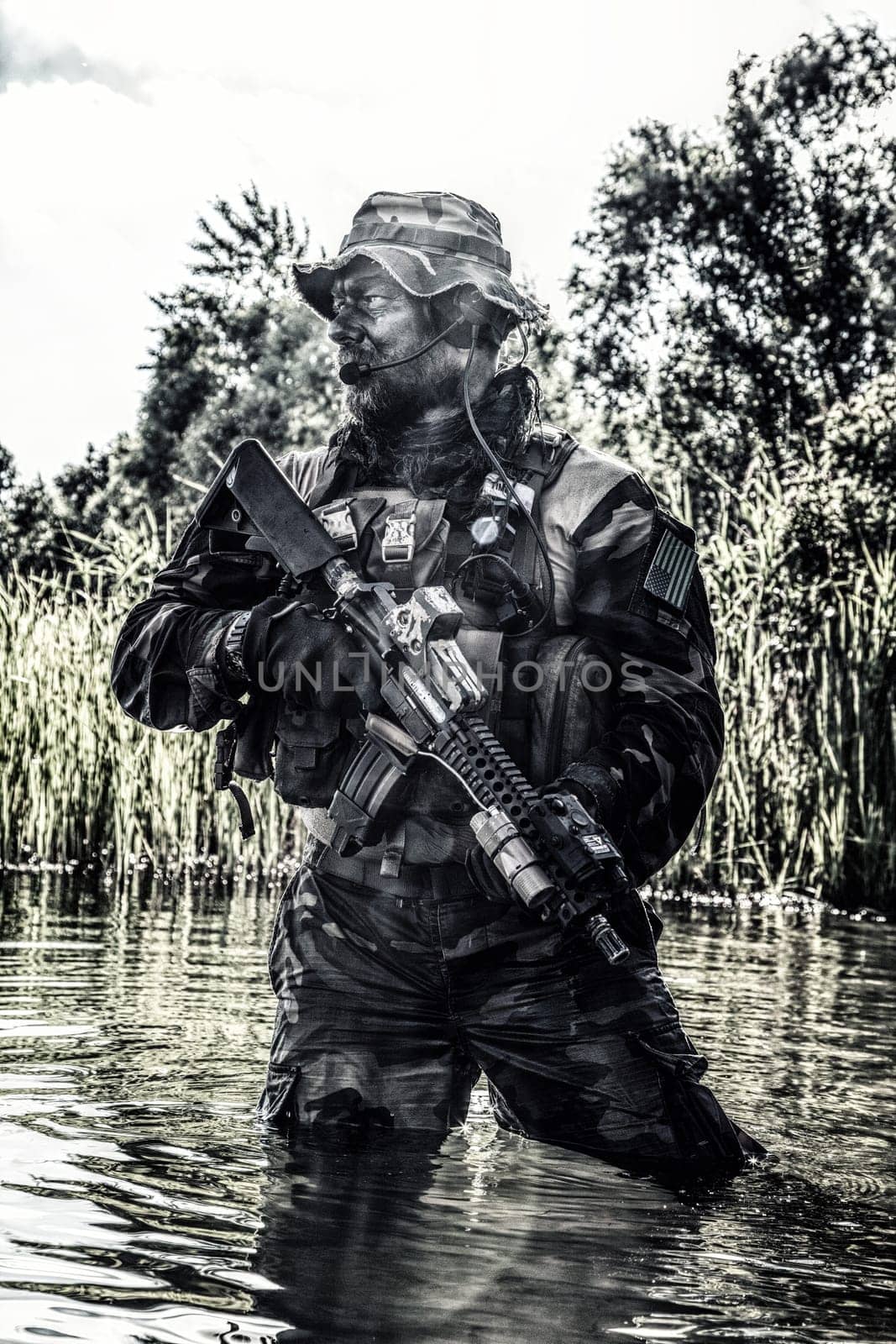Bearded soldier of special forces in action during river raid in the jungle terrain. He is waist deep in the water and mud and ready to meet enemy, survive and fight in agressive hostile environment