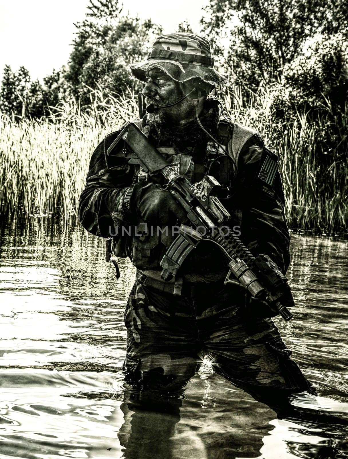 Bearded soldier of special forces in action during river raid in the jungle terrain. He is waist deep in the water and mud and ready to meet enemy, survive and fight in agressive hostile environment