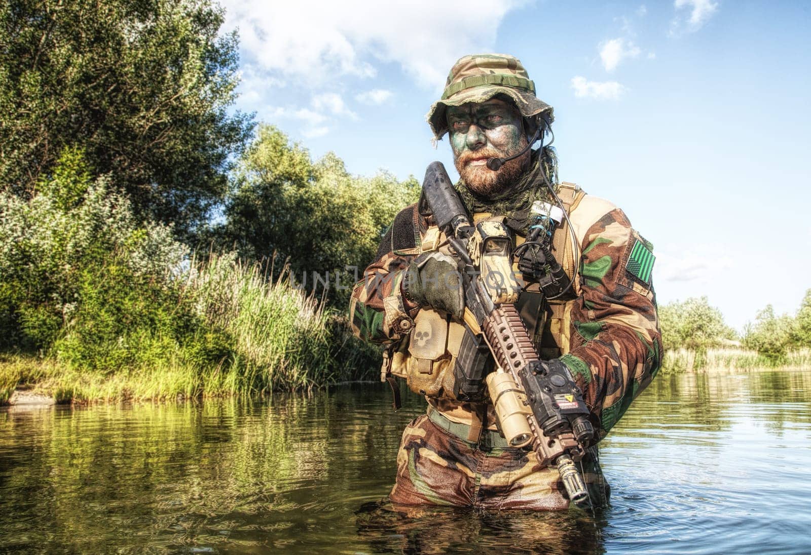 Bearded soldier of special forces in action during river raid in the jungle terrain. He is waist deep in the water and mud and ready to meet enemy, survive and fight in agressive hostile environment