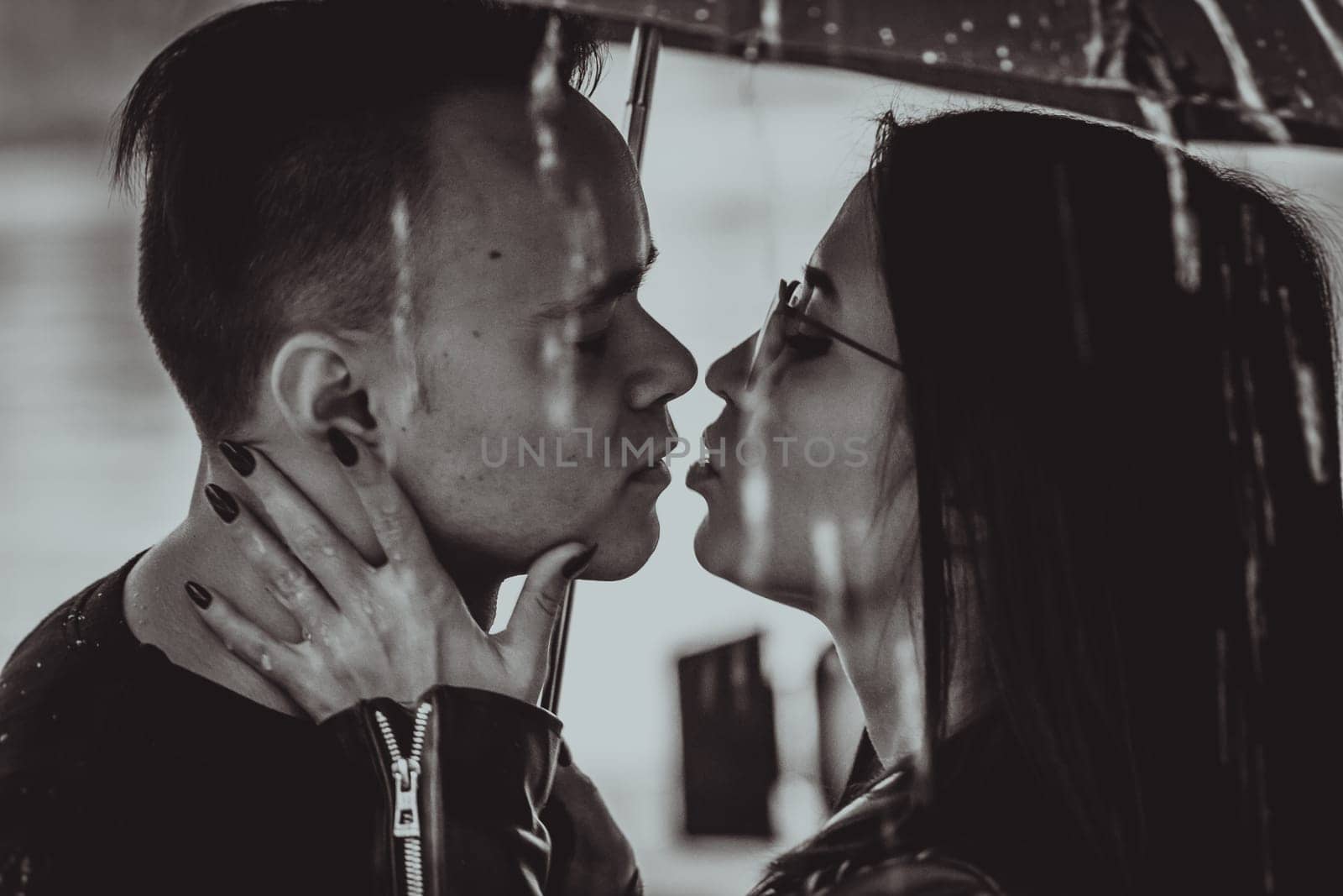 black white photo young couple standing under a dark umbrella.