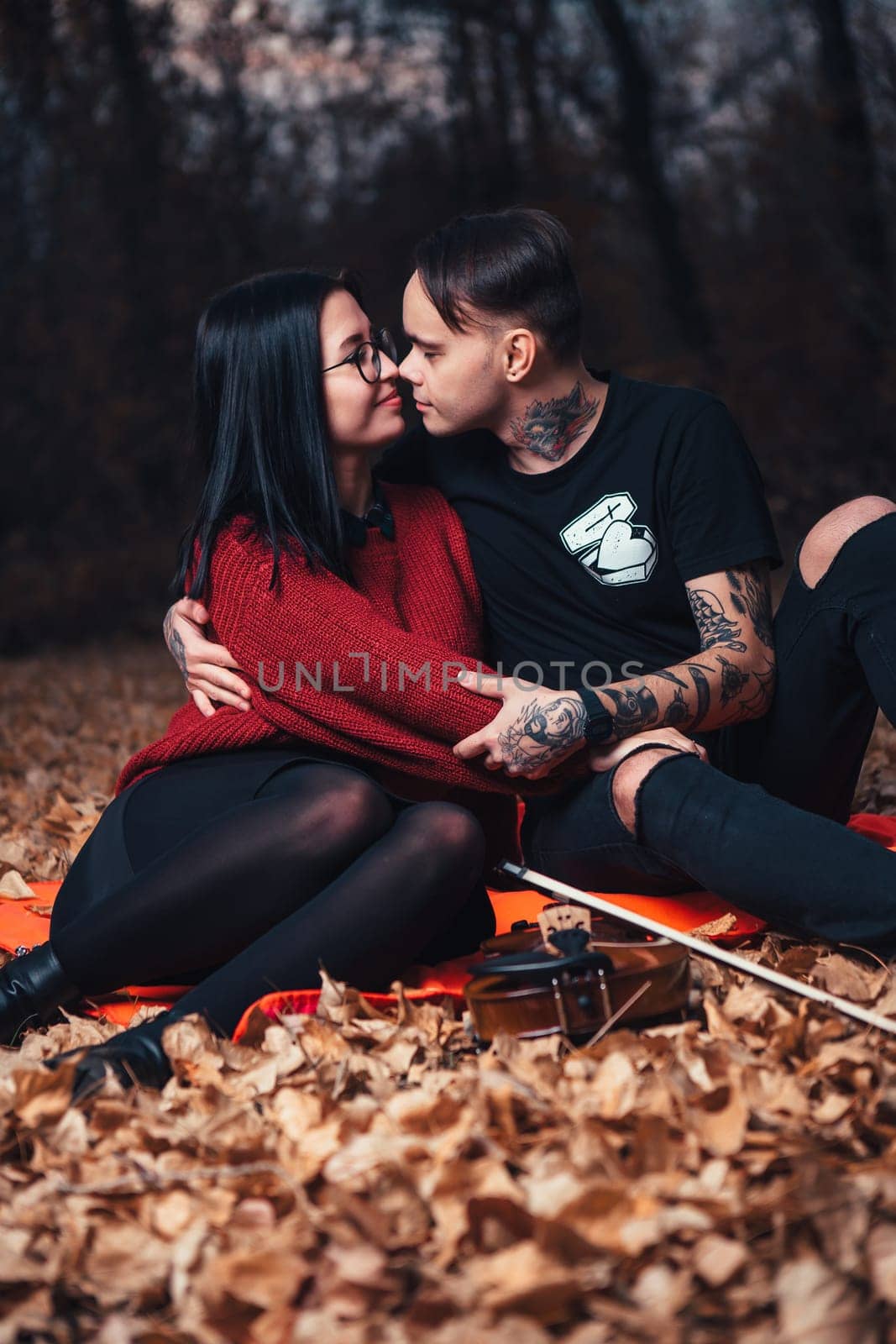 young man and young woman are sitting on a plaid in an autumn forest.