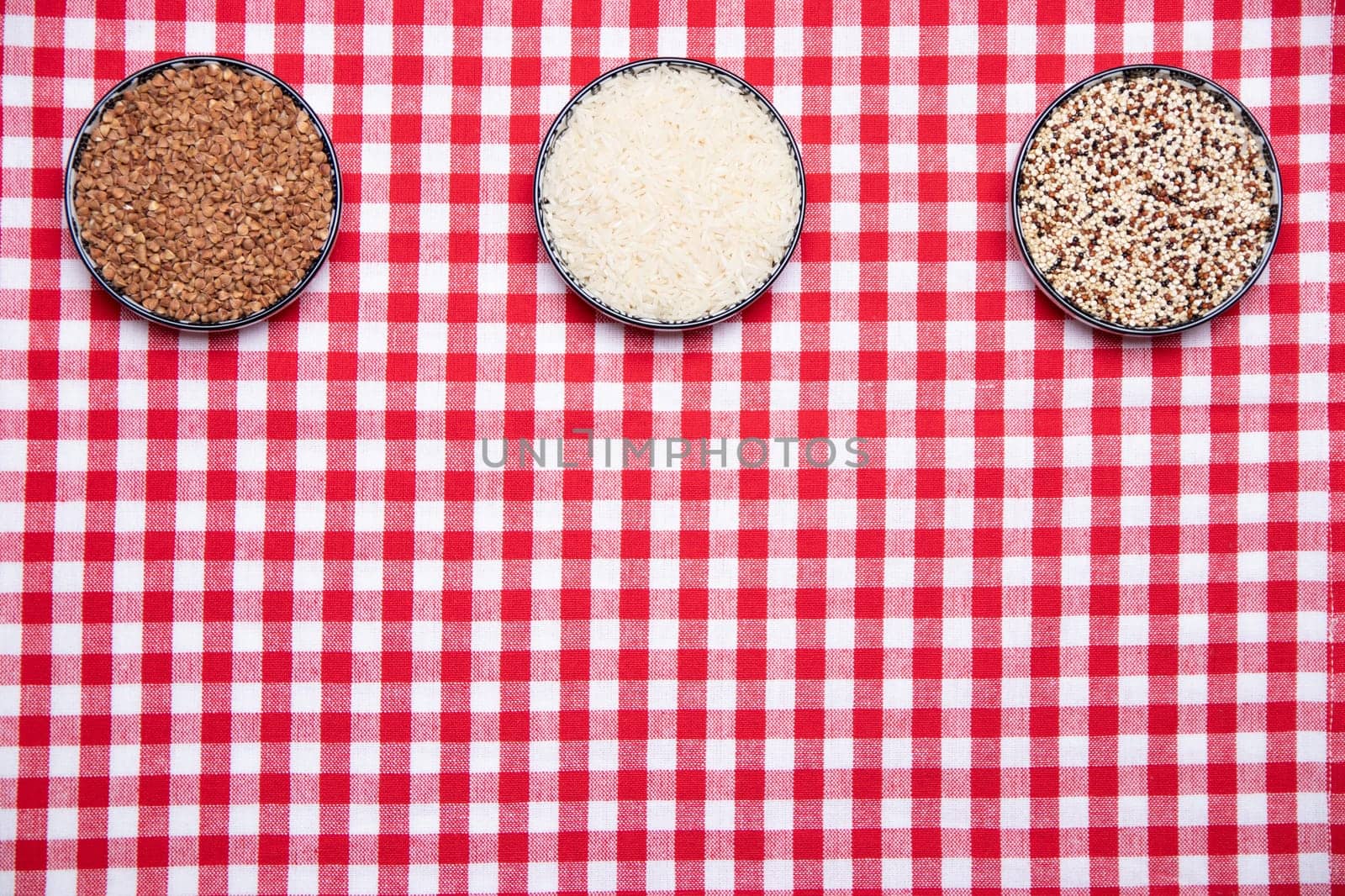 Vegetable food. A frame of three bowls with buckwheat, rice and quinoa on a red checkered tablecloth. Healthy eating. Top view with space for product montage.