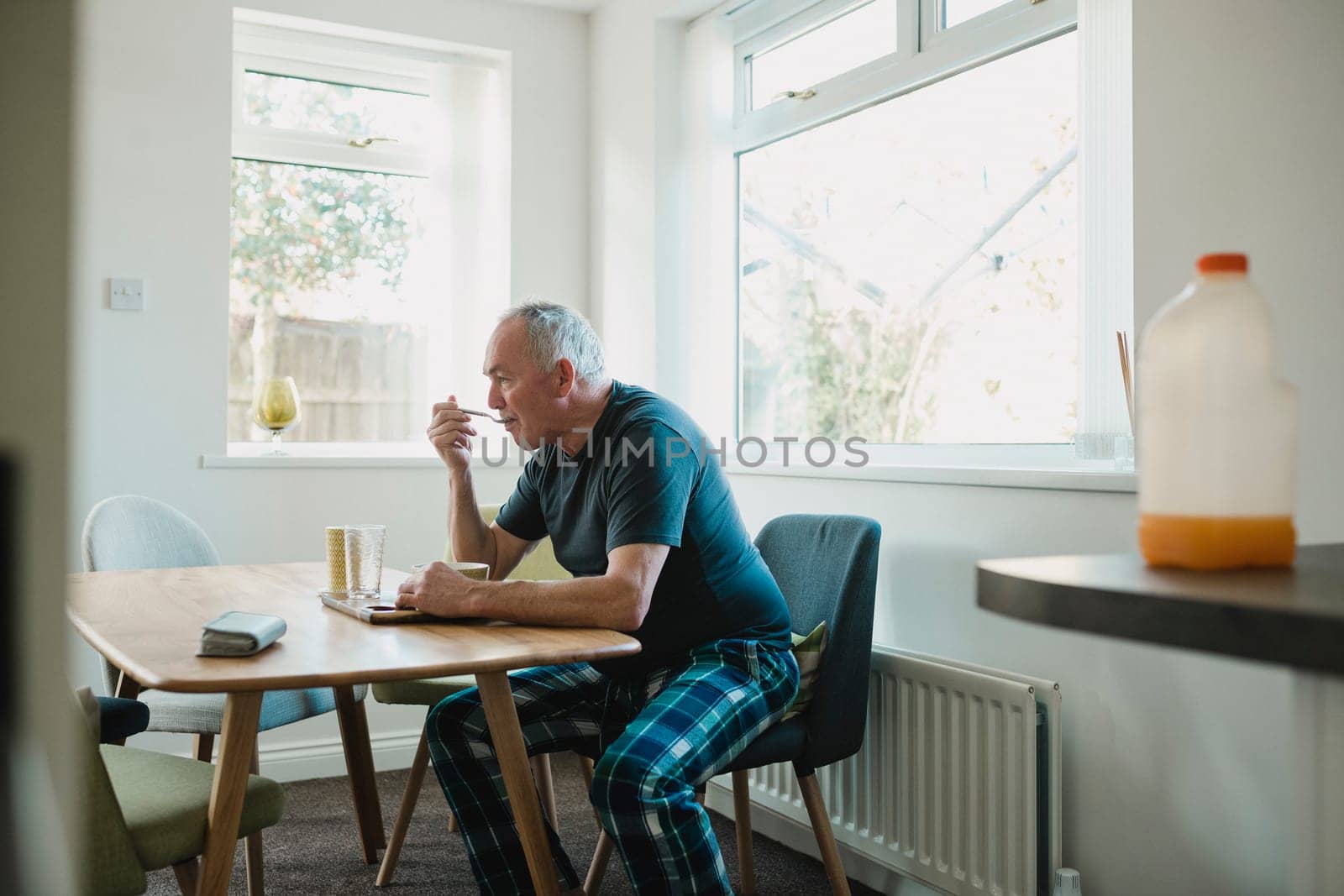 Senior man is sitting at the dining table in his home, enjoying a bowl of porridge for breakfast.