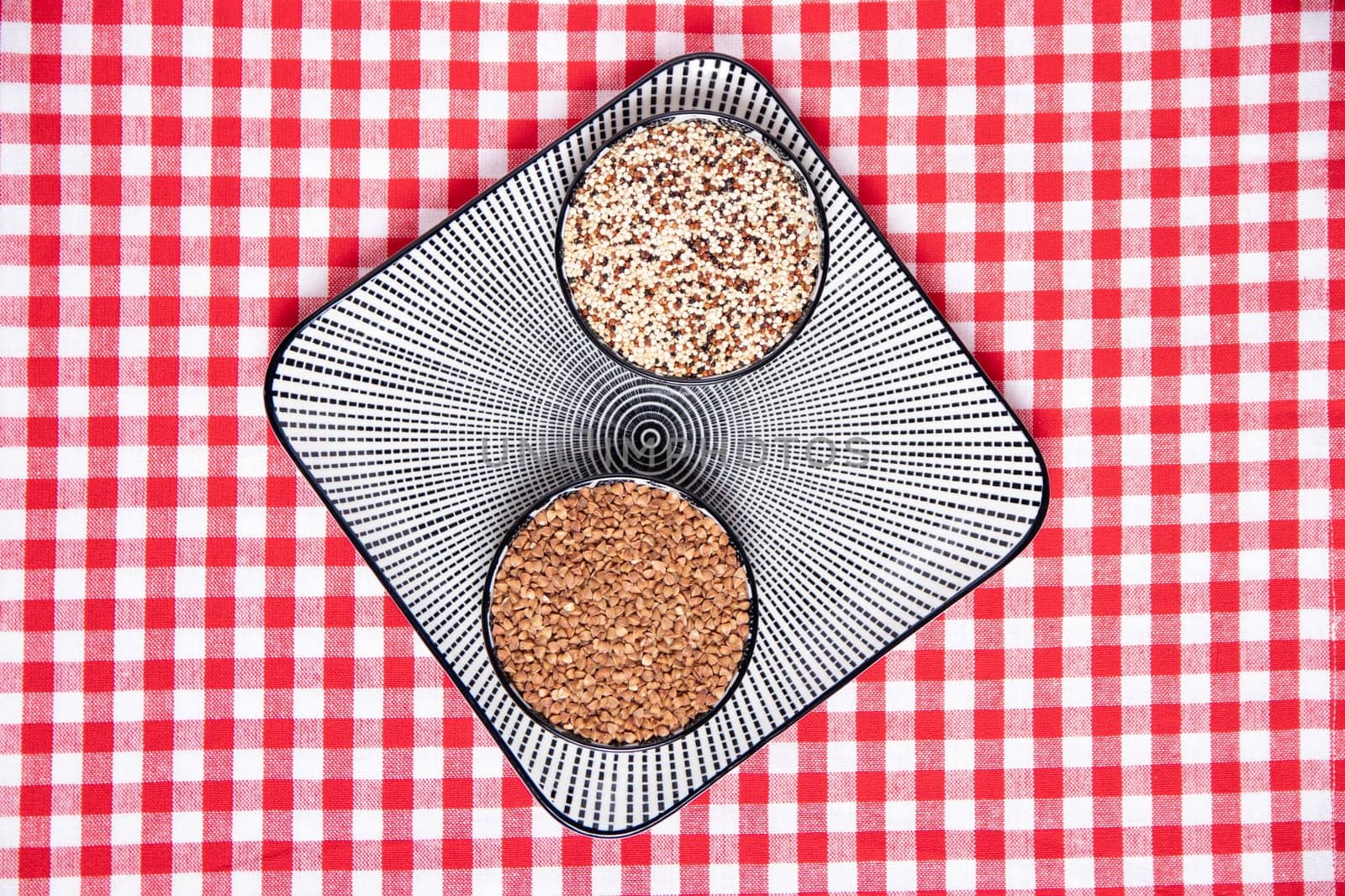 Vegetable food. A decorative plate with two bowls with buckwheat and quinoa on a red checkered tablecloth. Healthy eating. Top view with space for design.