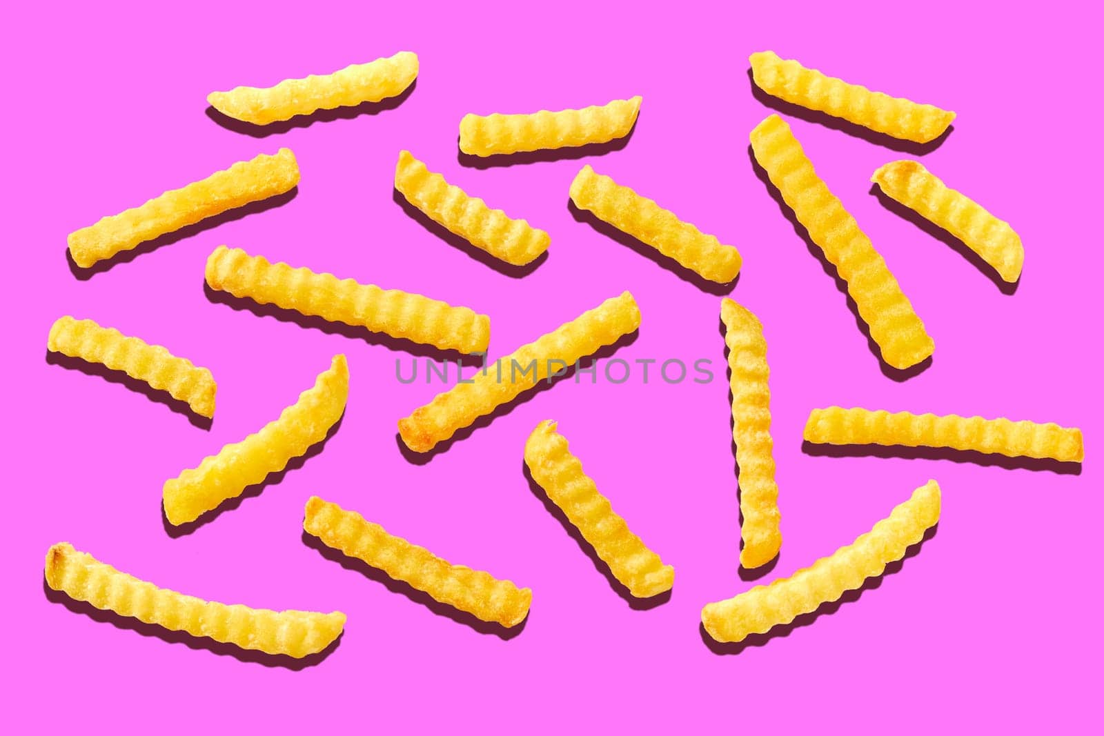 Pieces of fusilli pasta spread individually on pink background