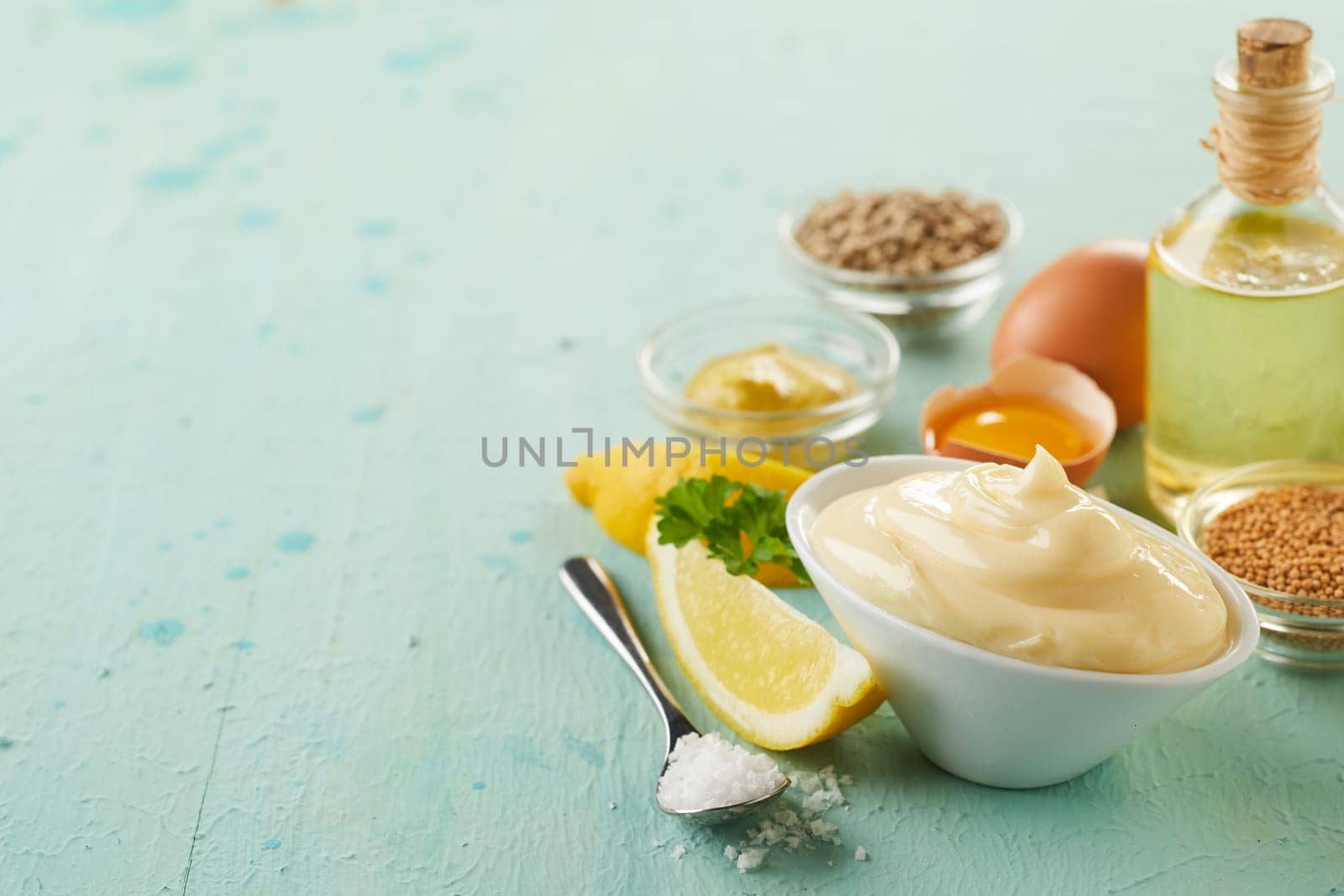 Bowl of delicious homemade mayonnaise with fresh ingredients including egg, oil and lemon on green wood with copy space