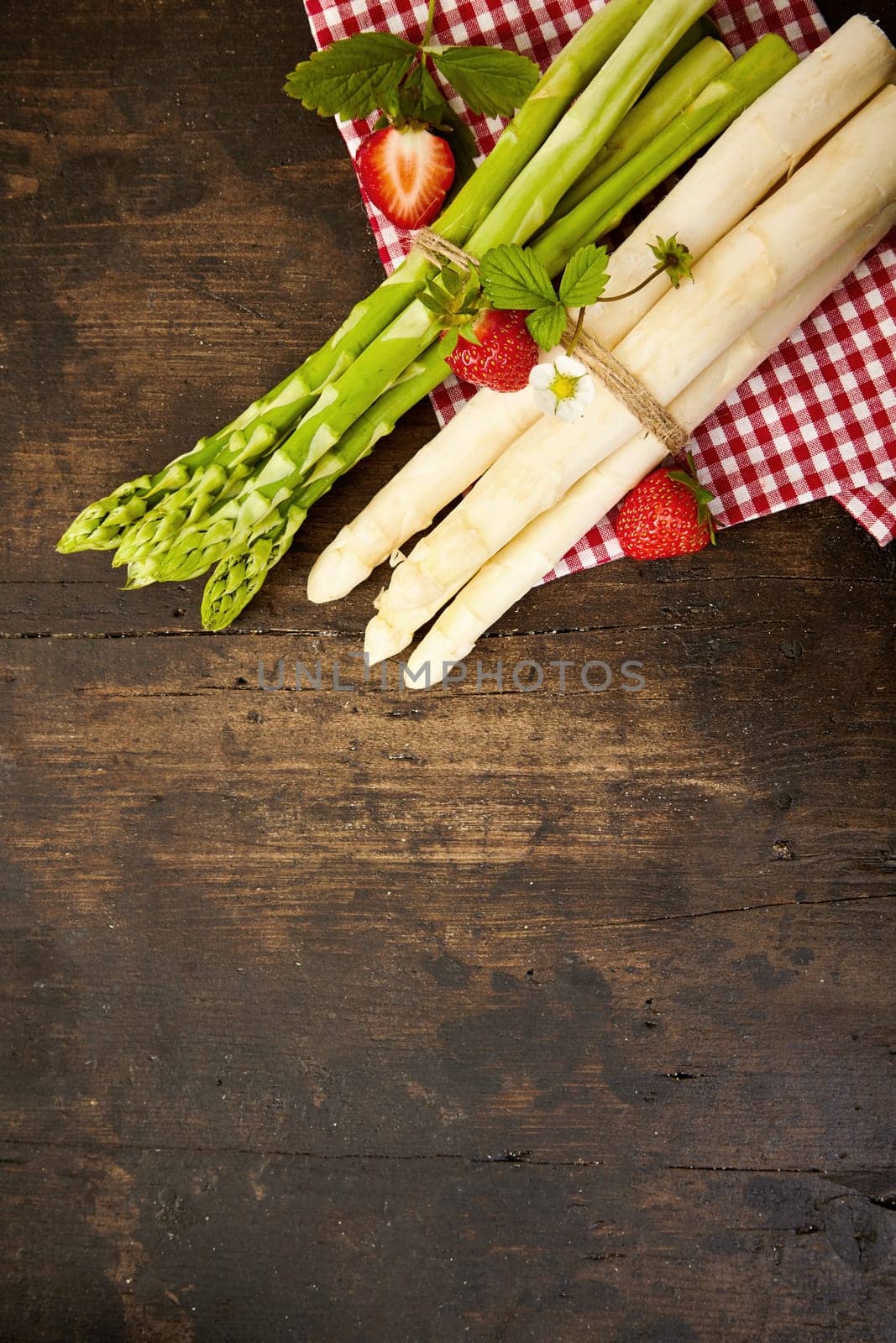Two bundles of fresh raw green and white asparagus spears tied with string on a checked red and white cloth on rustic wood with copy space