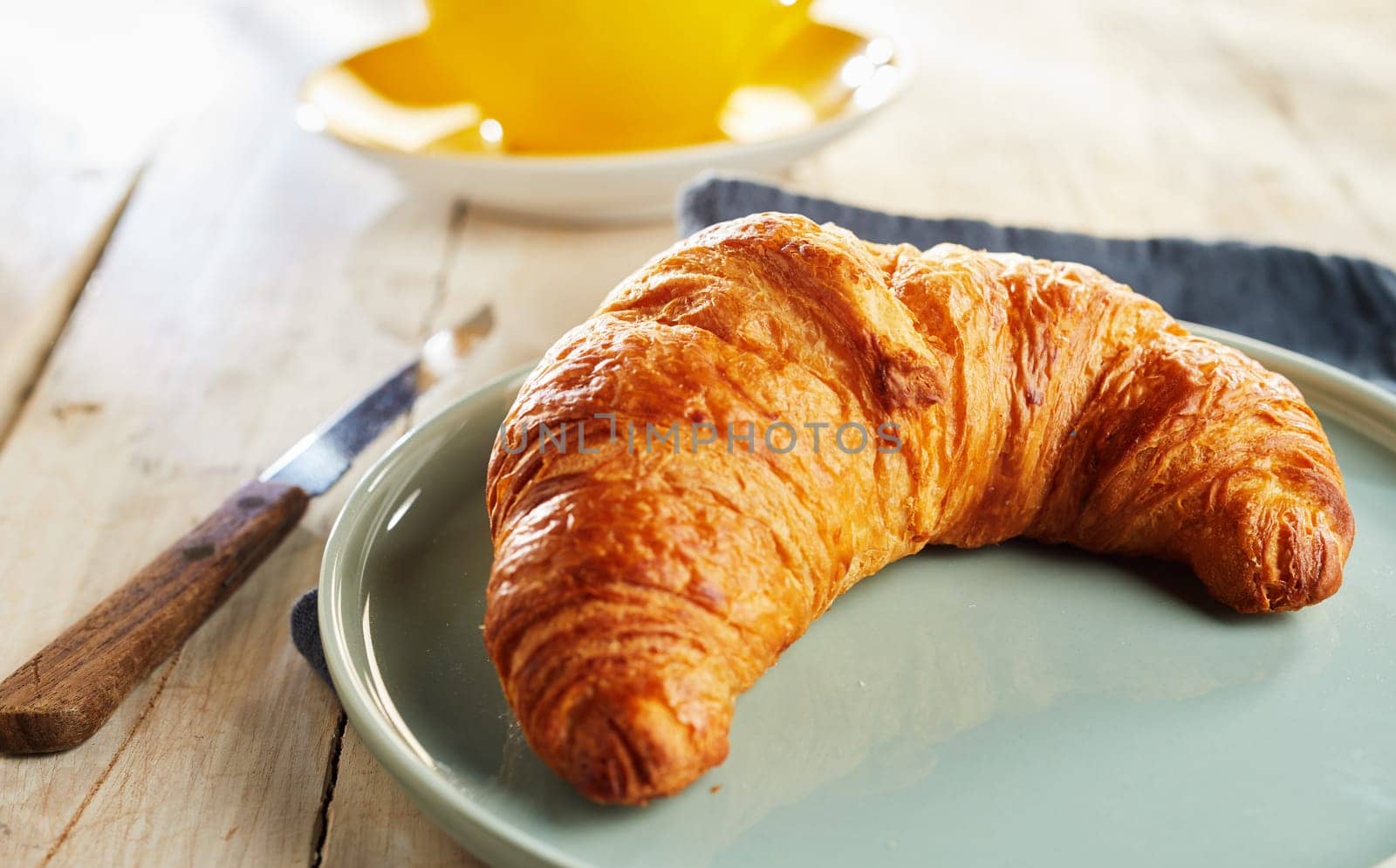 Fresh baked flaky French croissant served on plate with knife on wooden table, viewed in closeup