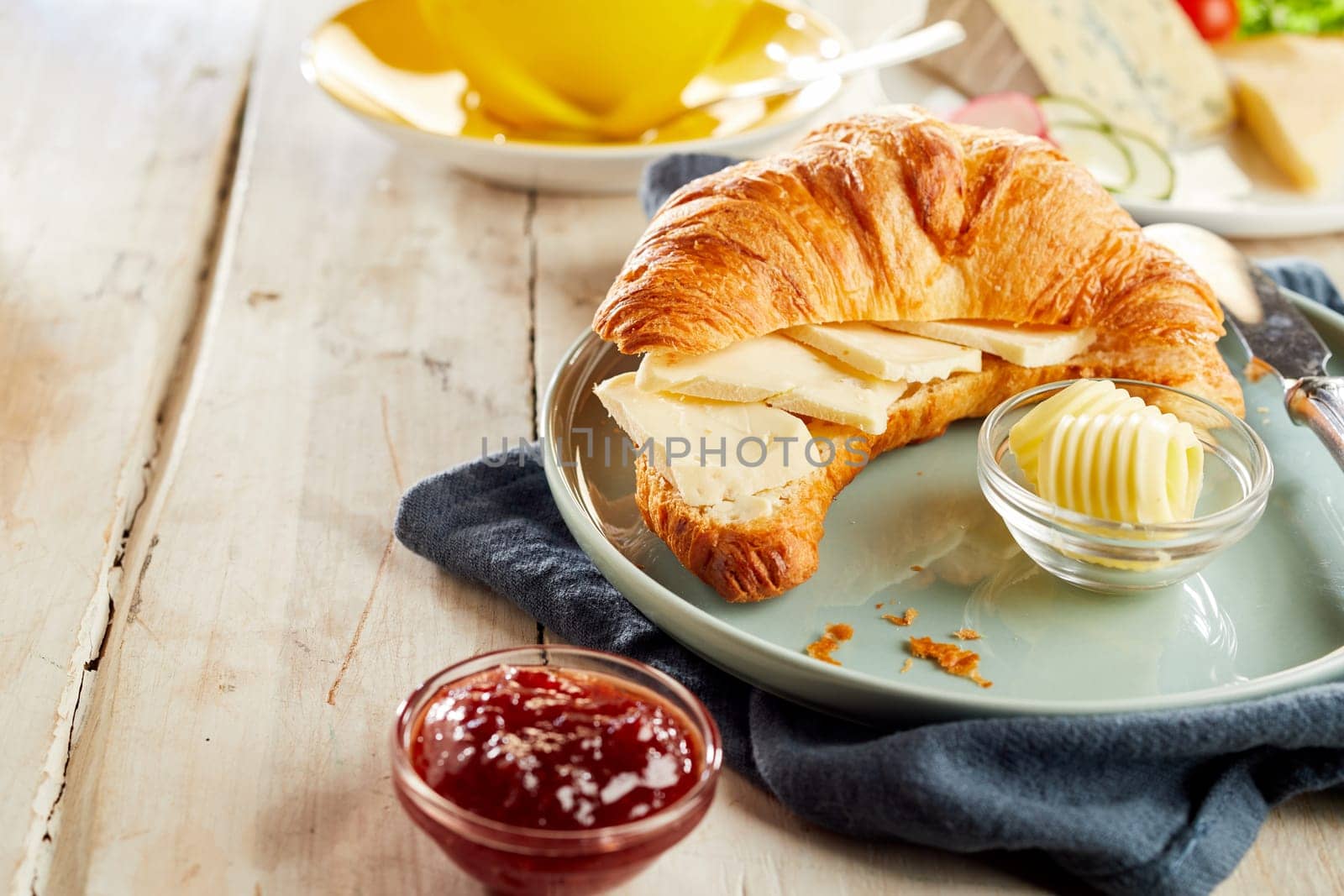 Croissant sliced in half, served with cheese, butter and ketchup in restaurant, on wooden table with copy space