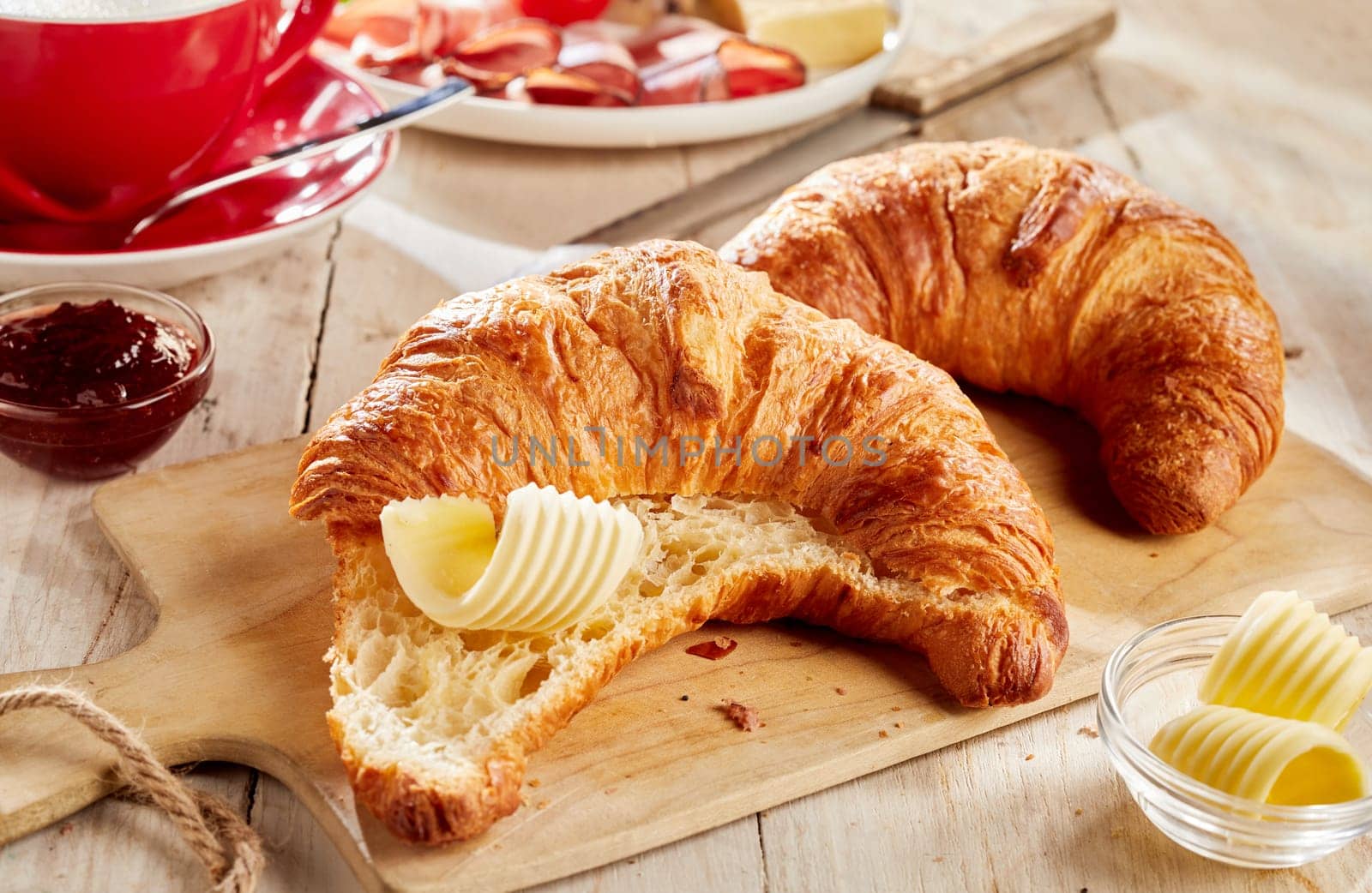 Sliced fresh baked croissant served with butter curls on wooden cutting board