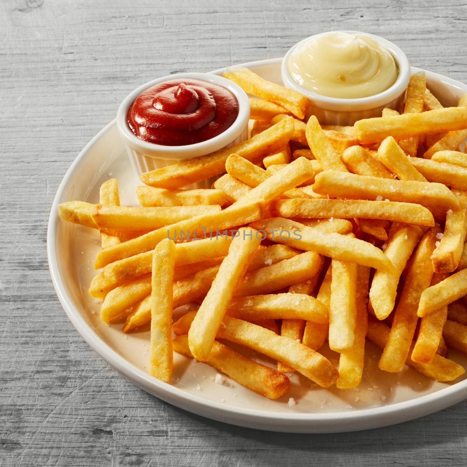 Plate of golden French fries, potato chips, or Pommes Frites served with little bowls of tomato sauce and mayonnaise in a close up view, square format