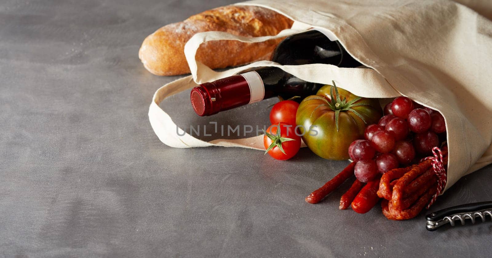 Food banner with groceries and wine in a reusable natural fiber carrier bag over a slate background with copy space to reduce the use of plastic bags