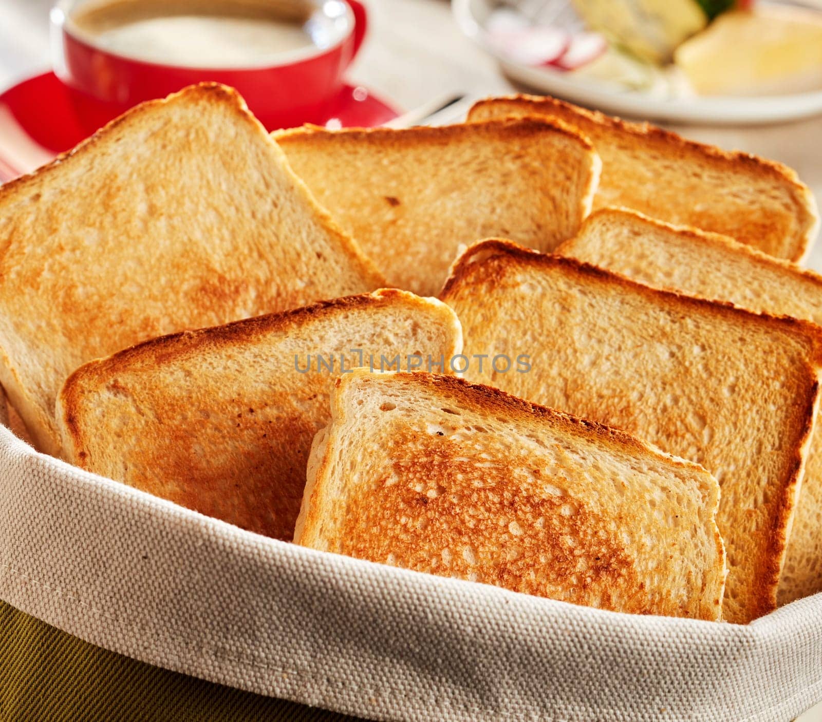 Close-up on fresh made crunchy bread toasts served in fabric bag. Cup of coffee blurred in background
