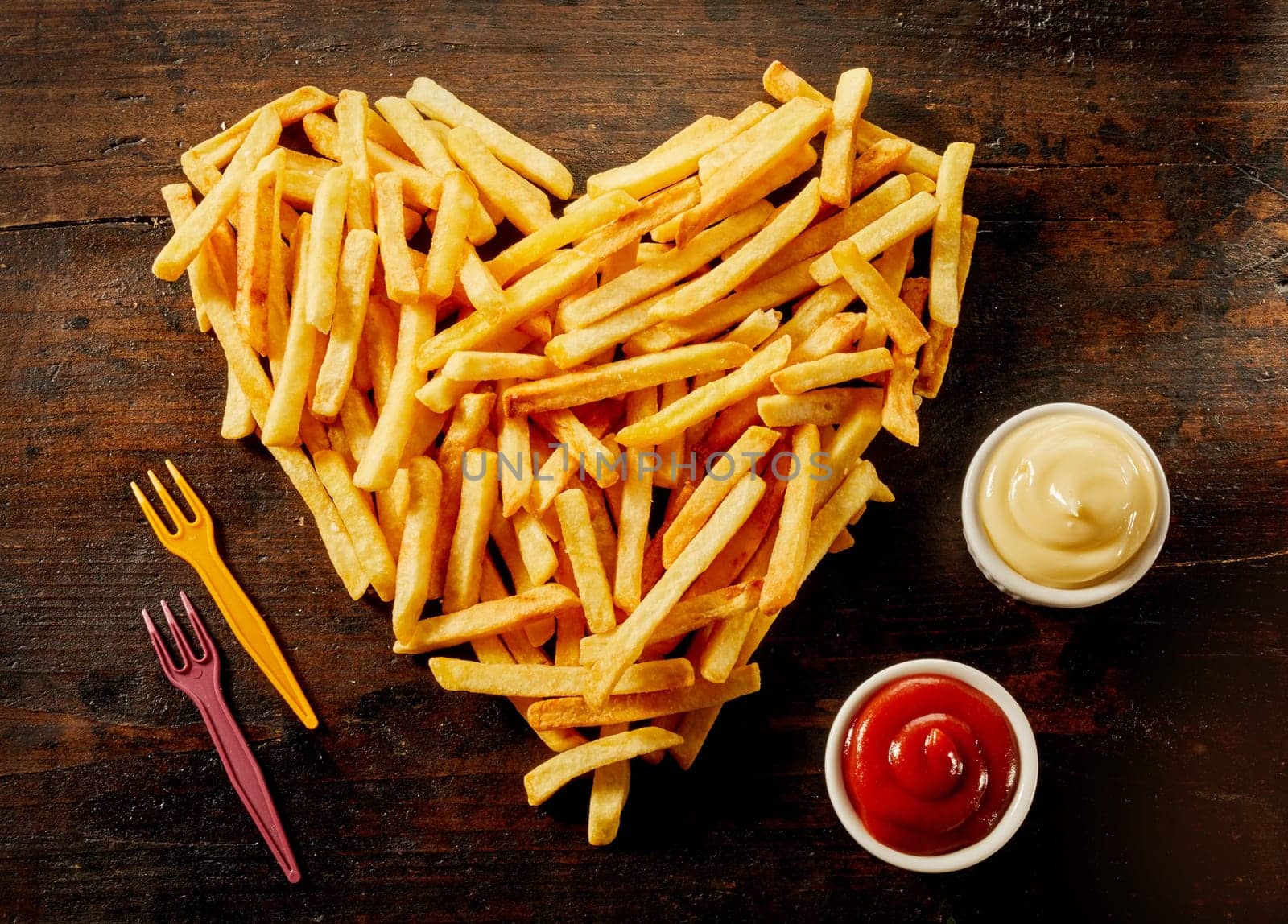 Heart shaped serving of French Fries with dips, dressings or sauce in small bowls alongside on wood