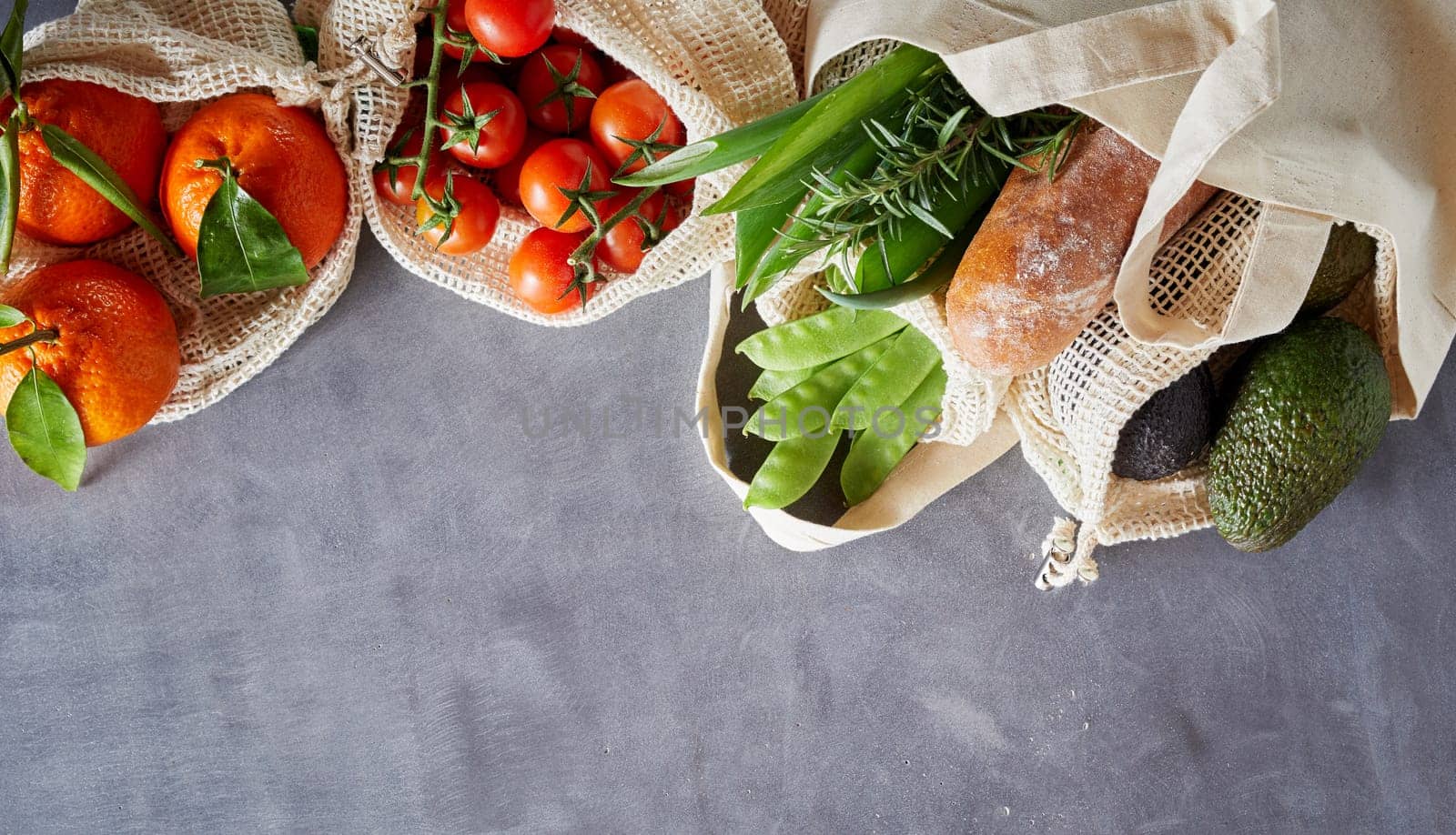 Fabric bags with fresh organic groceries from local market. Eco-friendly packing shopping concept with grey copy space