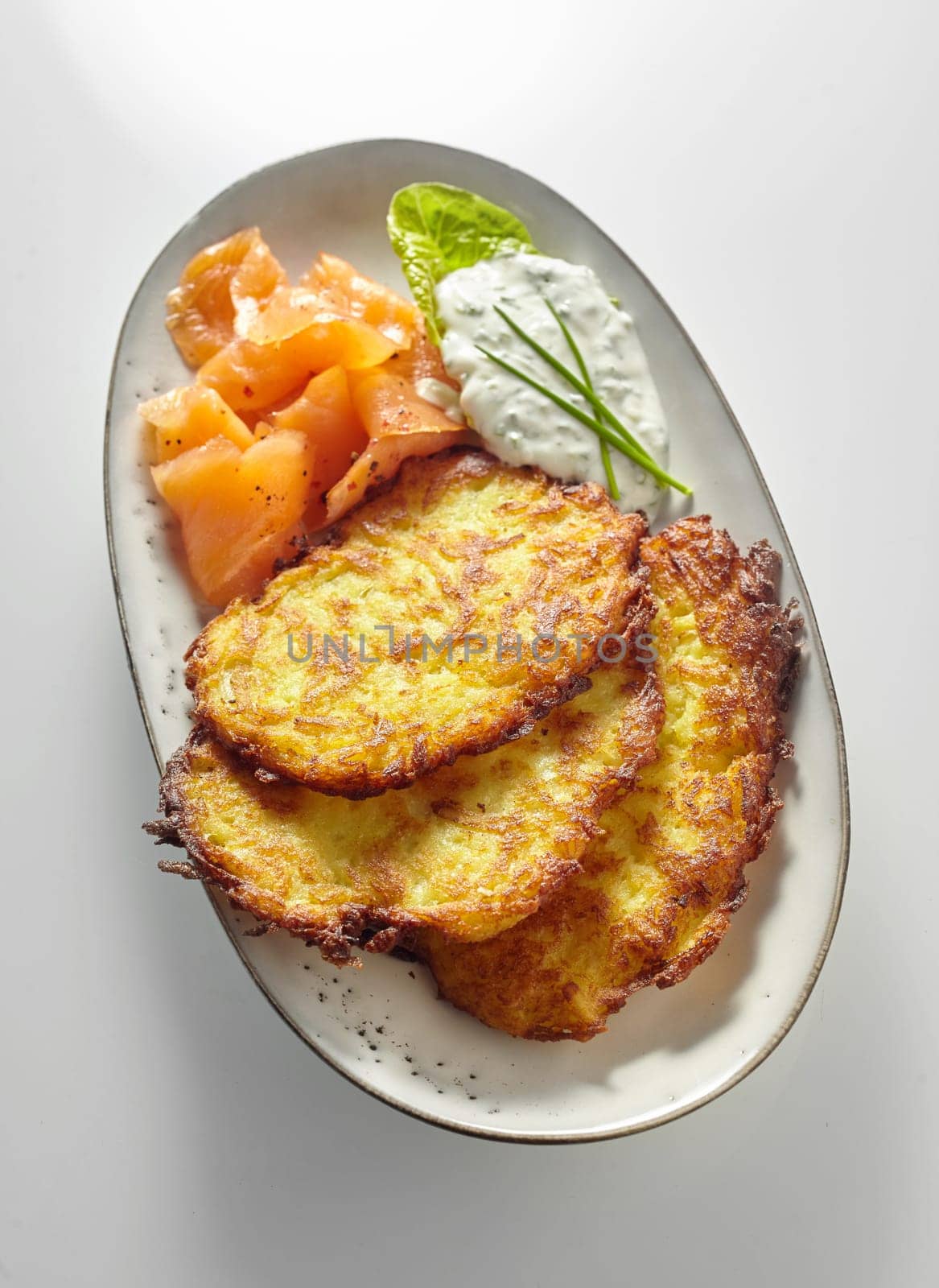 Serving of crispy golden German fried potato fritters with creamy sauce or dressing on an oval dish viewed from above