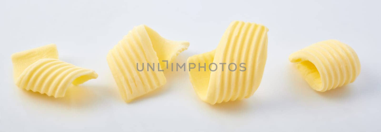 Set of different butter curls or rolls in a row in close-up on white surface background