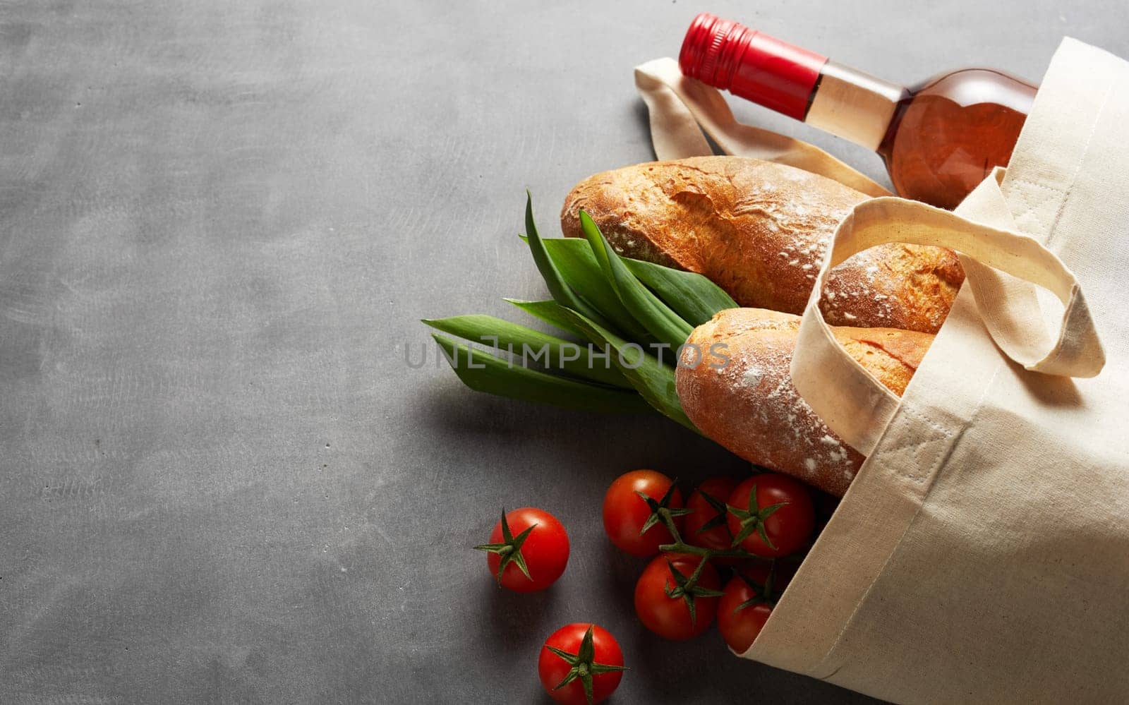 Natural fiber eco-friendly reusable shopping bag to save the planet from plastic pollution lying on slate filled with fresh groceries and wine