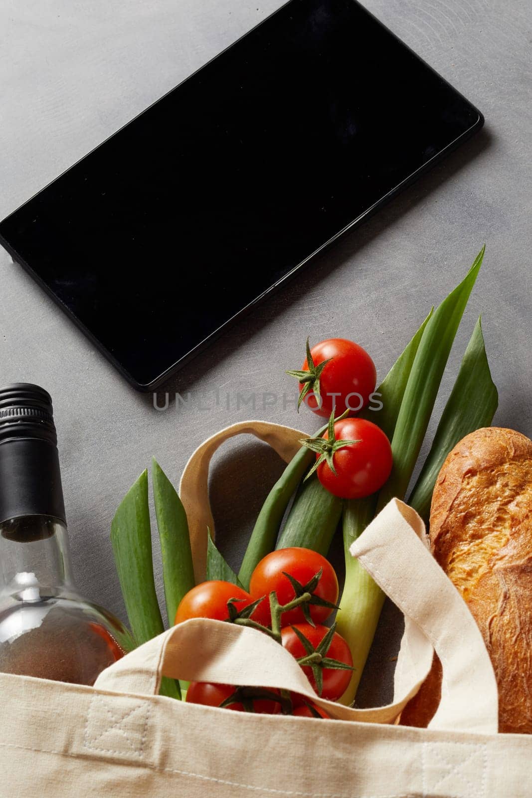 Fabric eco-friendly shopping bag with groceries, bottle of wine and tablet or mobile phone in a close up view conceptual of replacing plastic consumption
