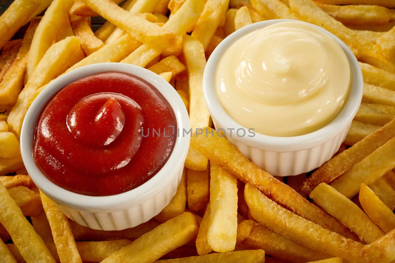 Side servings of tomato sauce or ketchup and mayonnaise on a background of golden crisp fired potato chips, French fries or Pommes Frites
