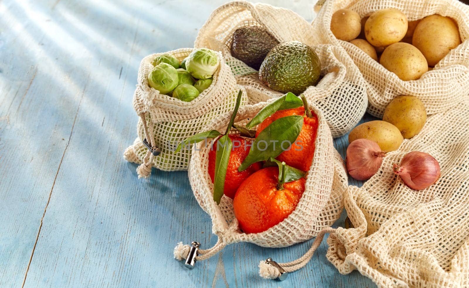 Groceries from country market, fresh fruits and organic vegetables in eco-friendly reusable net bags, placed on wooden table and viewed in close-up with copy space