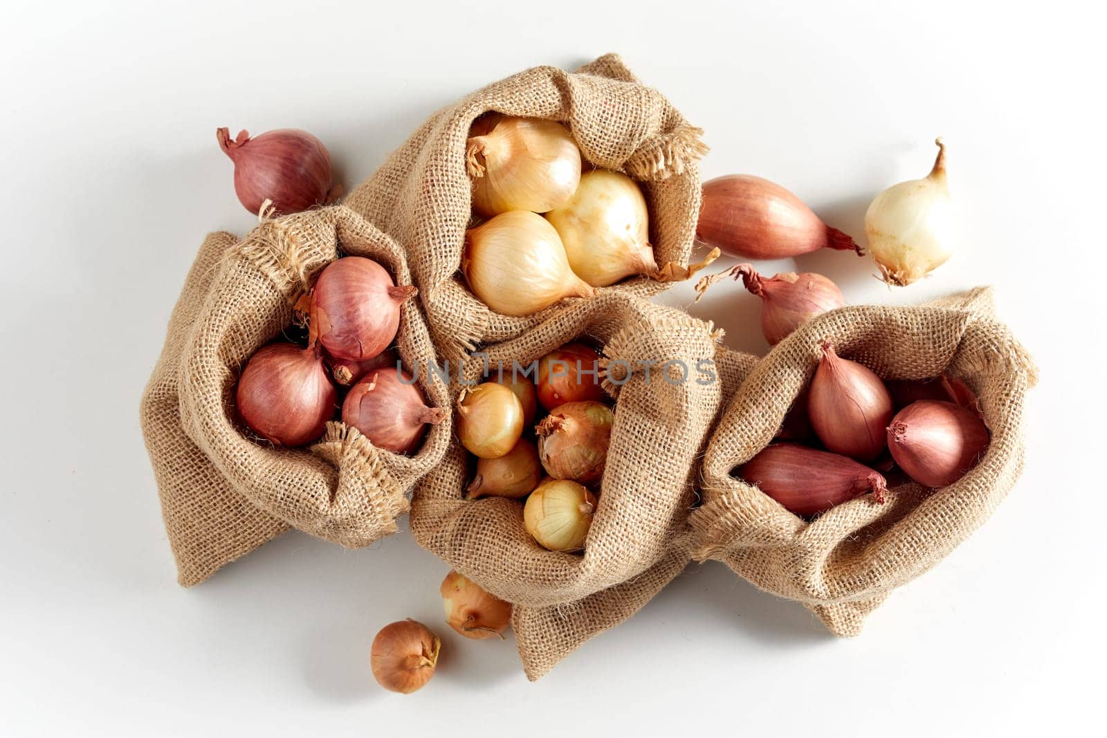 Burlap sack bags with various onions from local market, viewed from above and isolated on white background with shadow