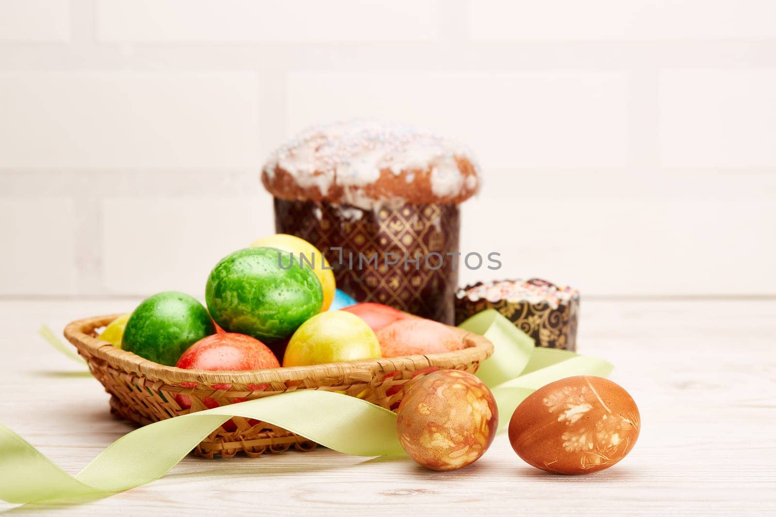 Still life with colored easter eggs and easter cakes lying on a wooden table on light background with copy space. Greeting card. Selective focus on eggs
