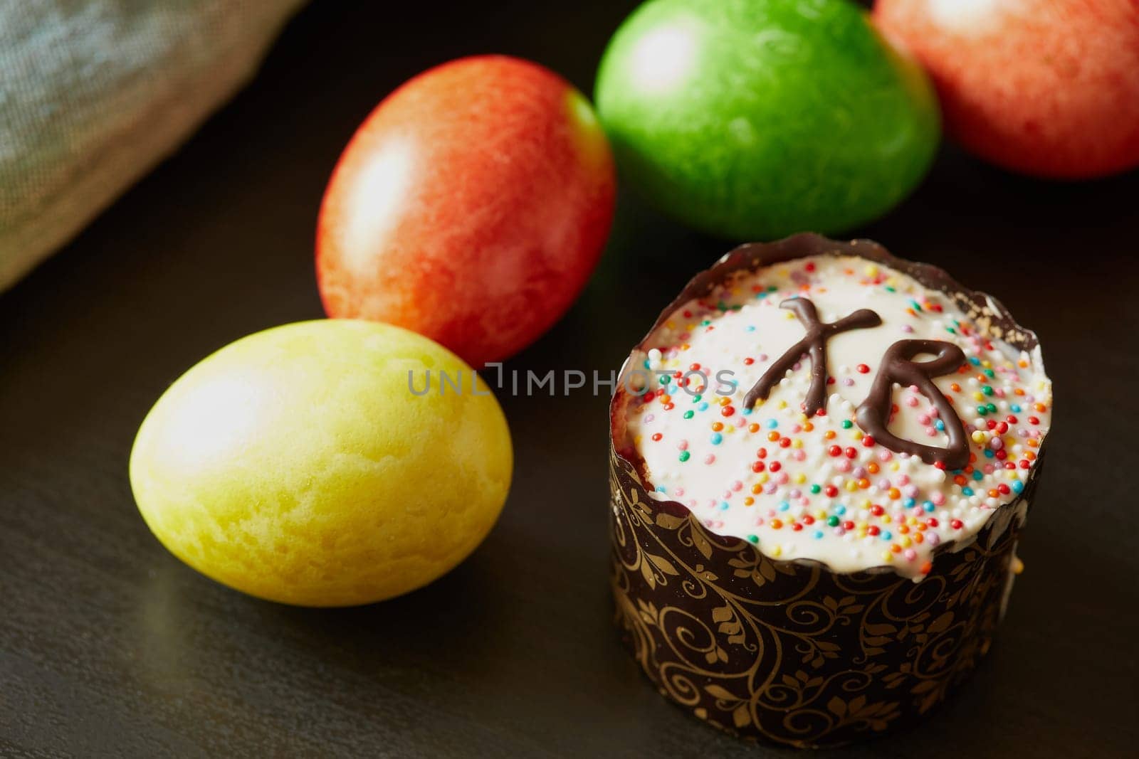 Still life with colored easter eggs and easter cake lying on black background. Greeting card. Selective focus on easter cake