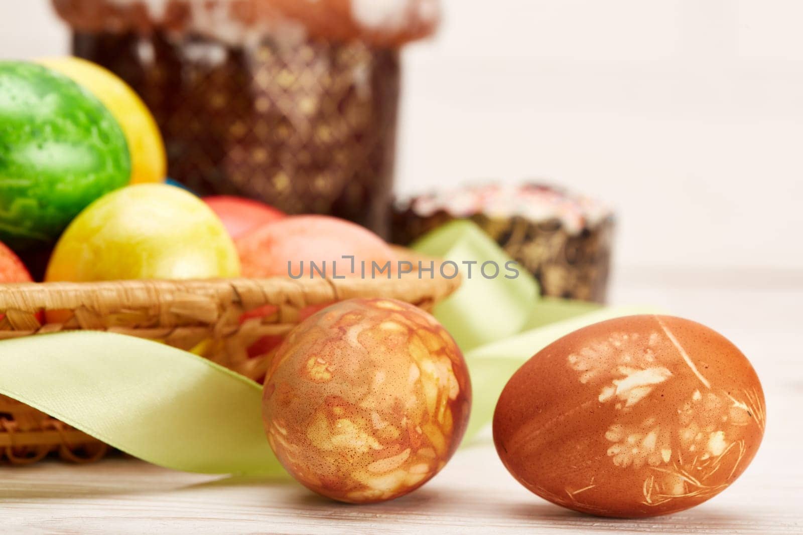 Still life with colored easter eggs and easter cakes lying on a wooden table on light background. Greeting card. Selective focus on eggs