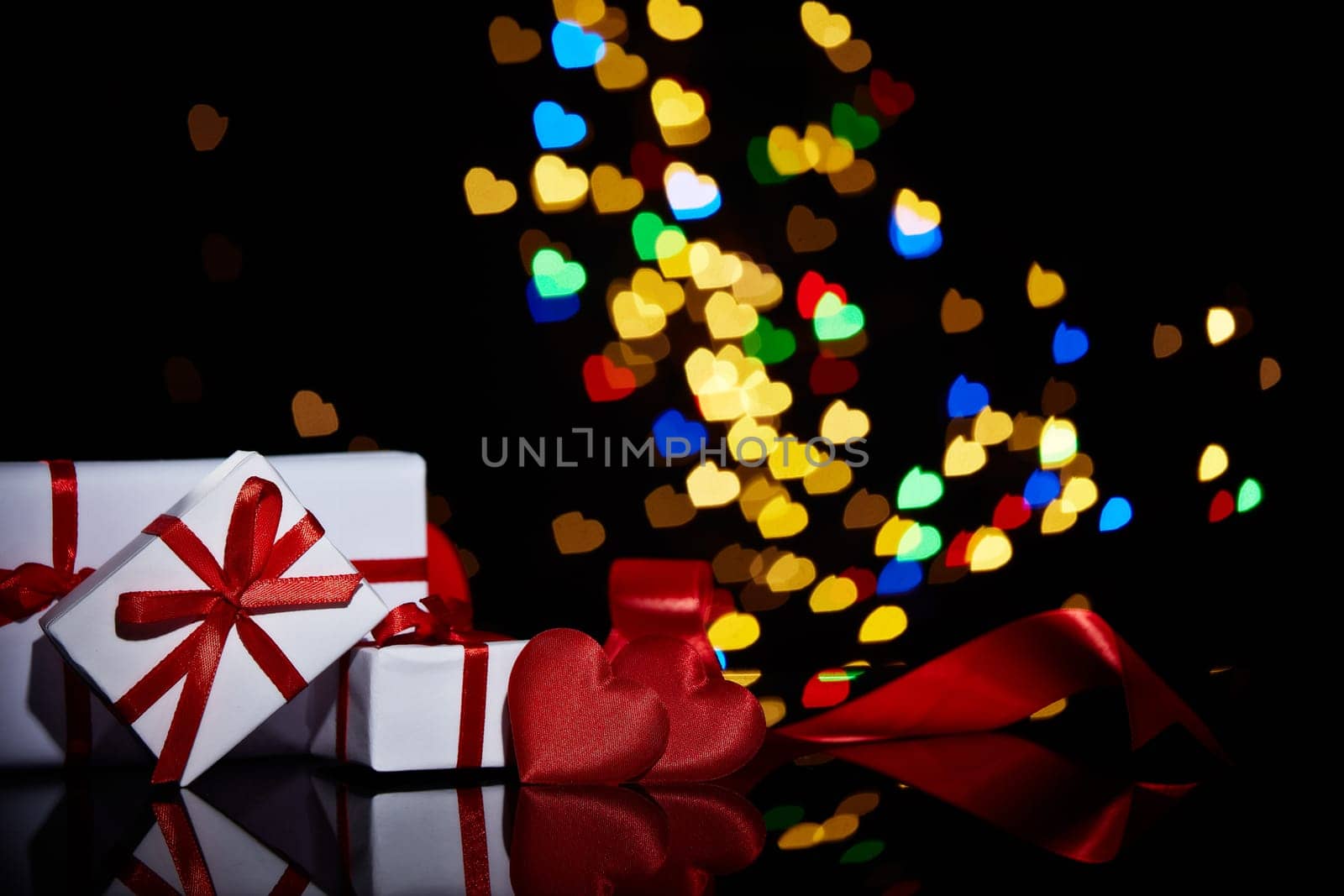 Gift boxes and red satin hearts on a black background with heart-shaped bokeh . Valentine's Day card with copy space. Design element for romantic greeting card, wedding invitation