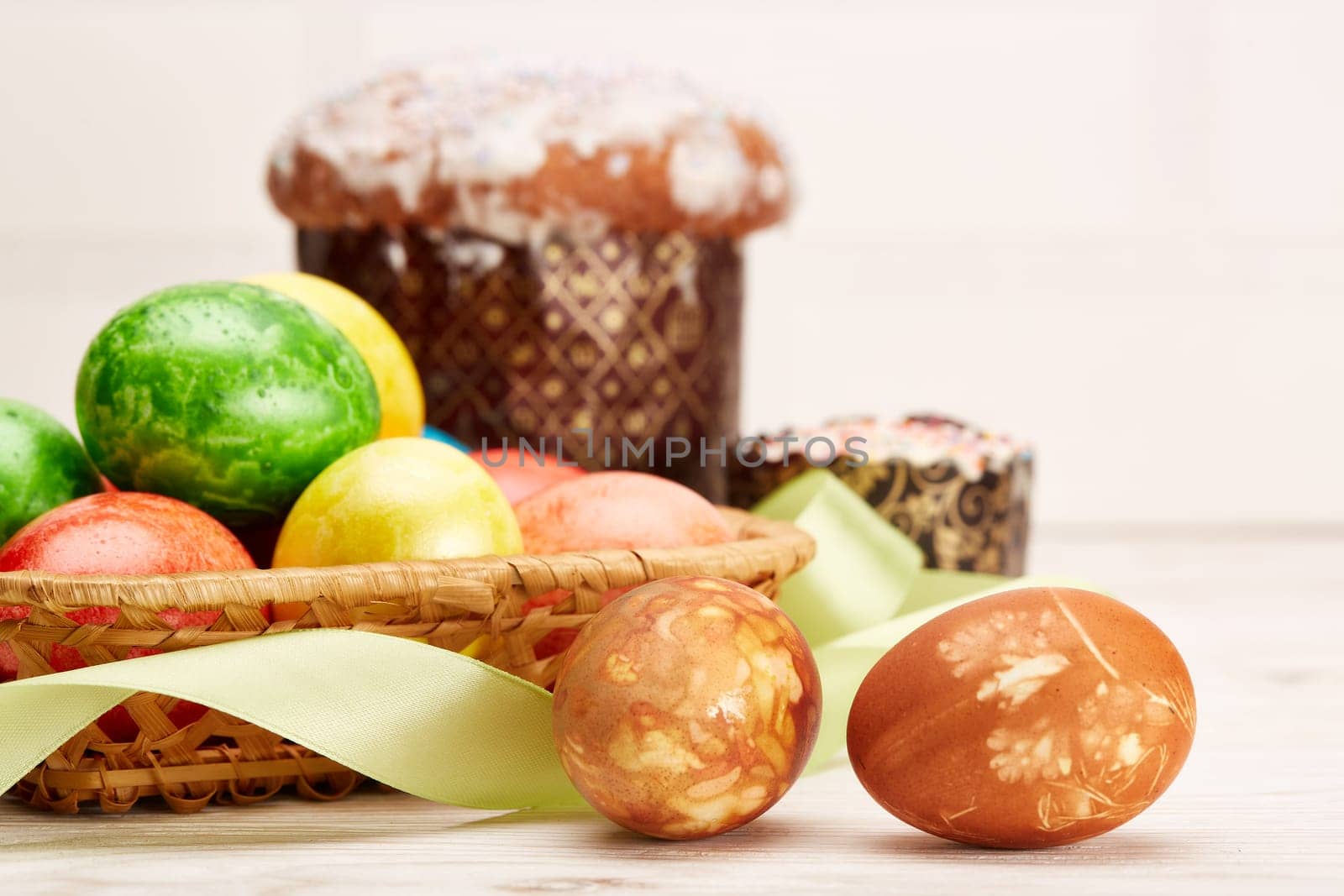 Still life with colored easter eggs and easter cakes lying on a wooden table on light background. Greeting card. Selective focus on eggs