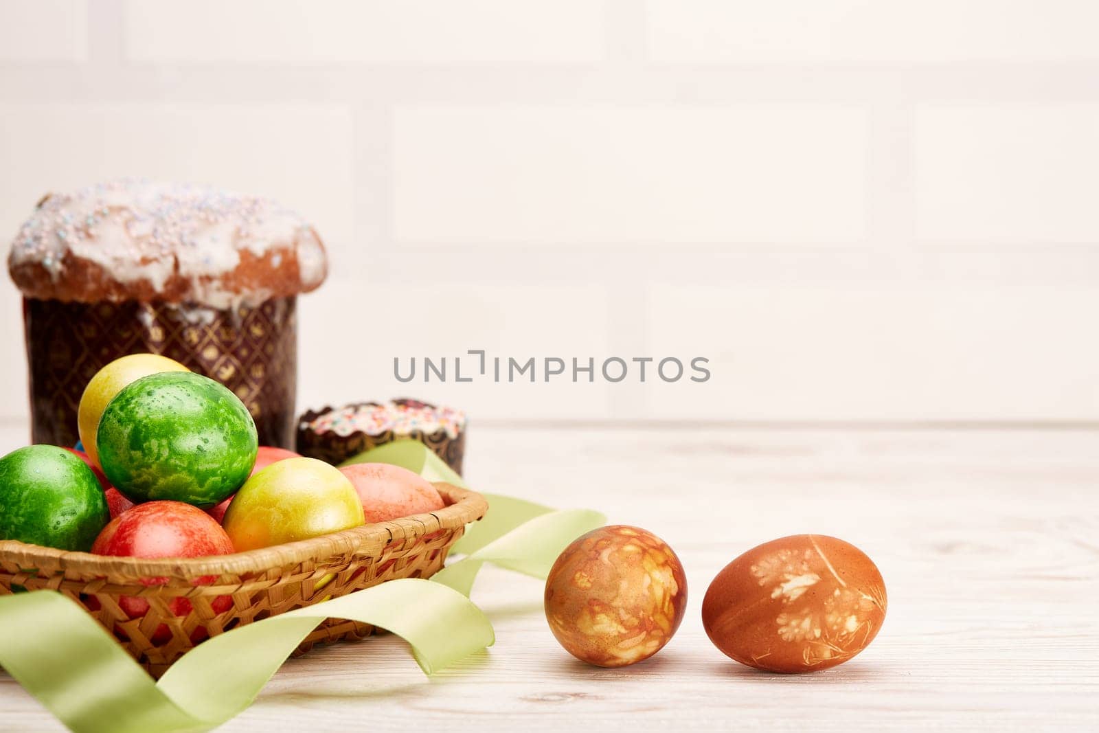 Still life with colored easter eggs and easter cakes lying on a wooden table on light background with copy space. Greeting card. Selective focus on eggs