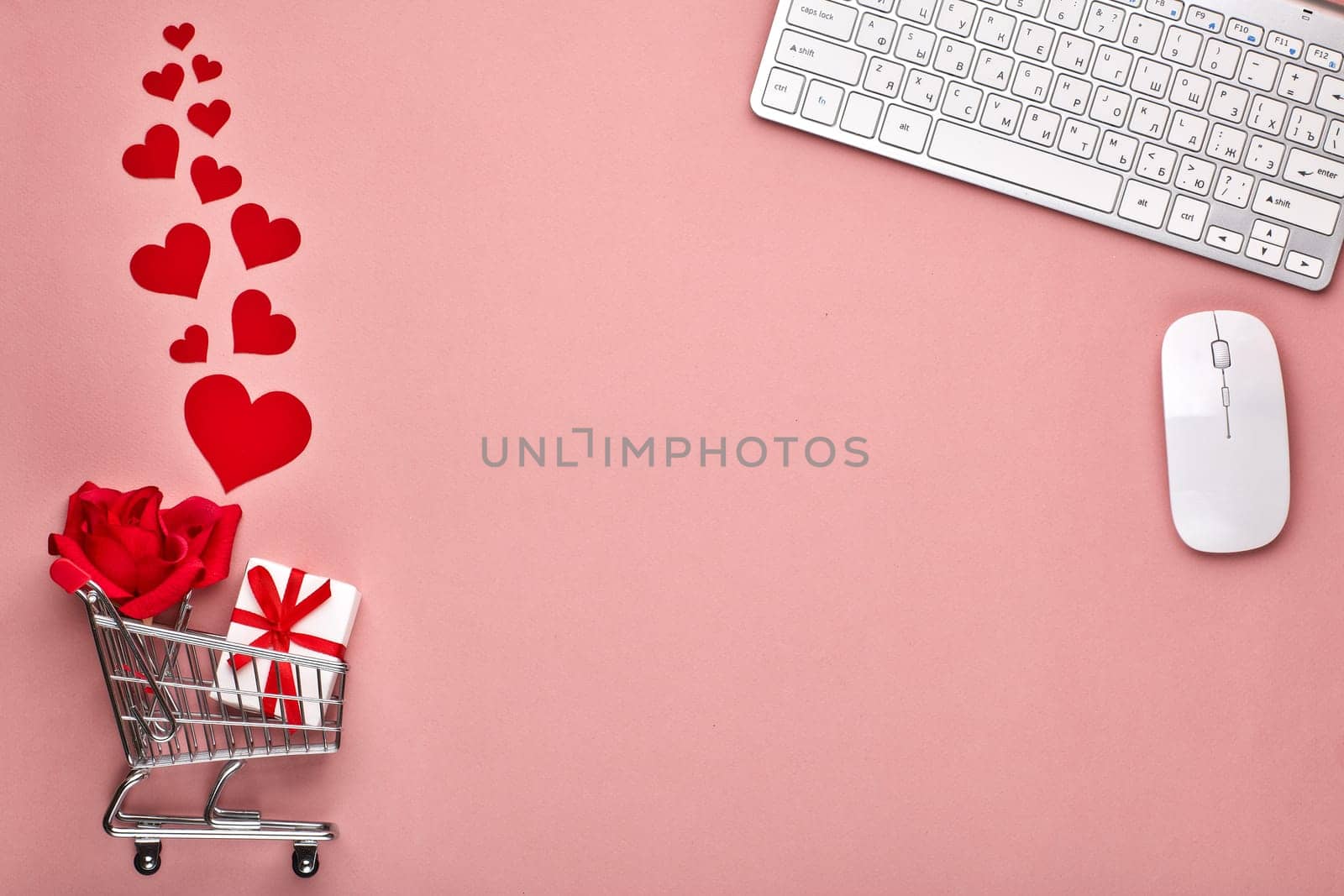 Shopping trolley, Computer keyboard and mouse, gift box, flower and decorative red hearts on pink background with copy space. Concept of internet shopping. Valentine's day, Mother's day, wedding