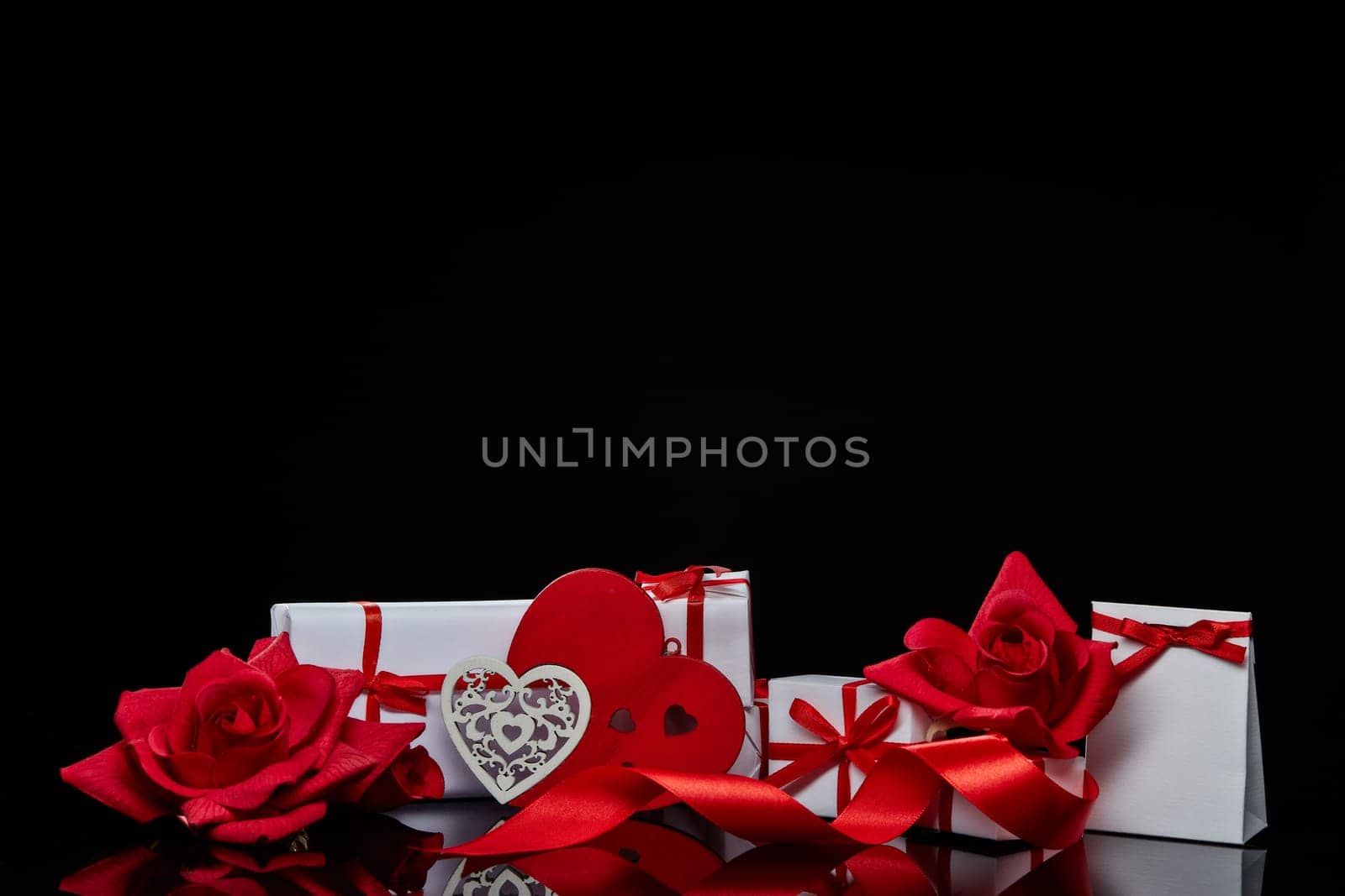 Gift boxes and red roses and decorative heart on black background. Valentine's Day card with copy space. Design element for romantic greeting card, wedding invitation