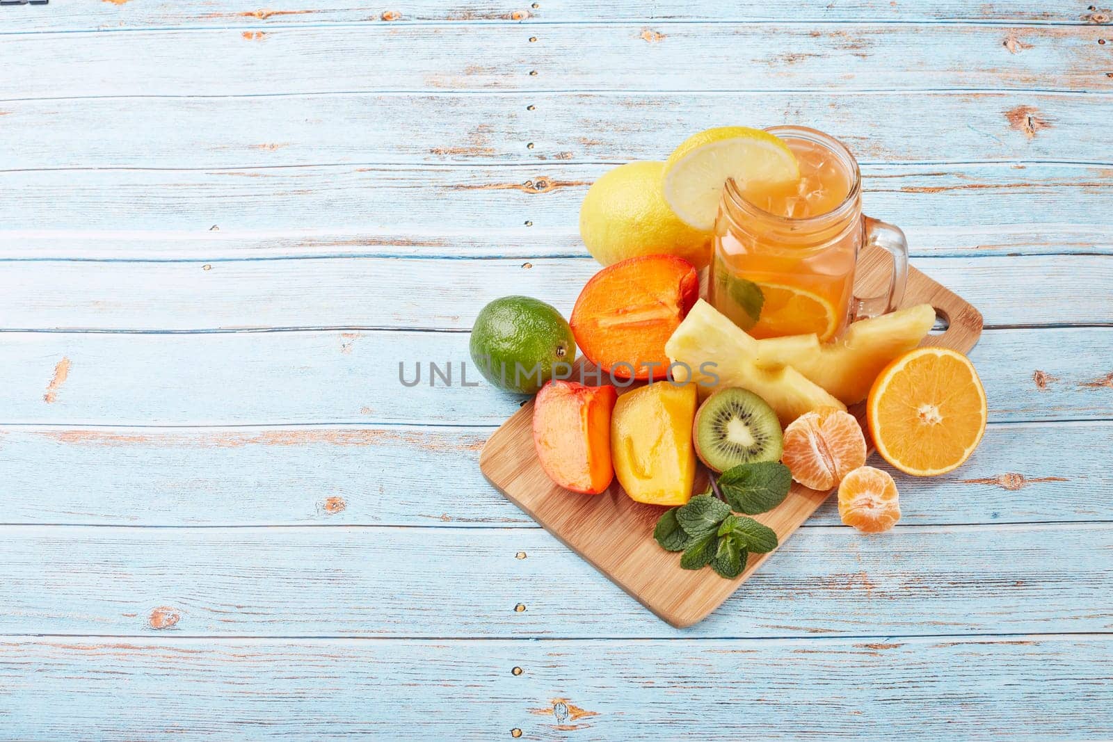 Fruit lemonade with ice, leaves of mint, lemon, pineapple, mango and lime slices standing on blue wooden table. Homemade lemonade with mix fruits. Healthy cool beverage, fruit juice. Top view